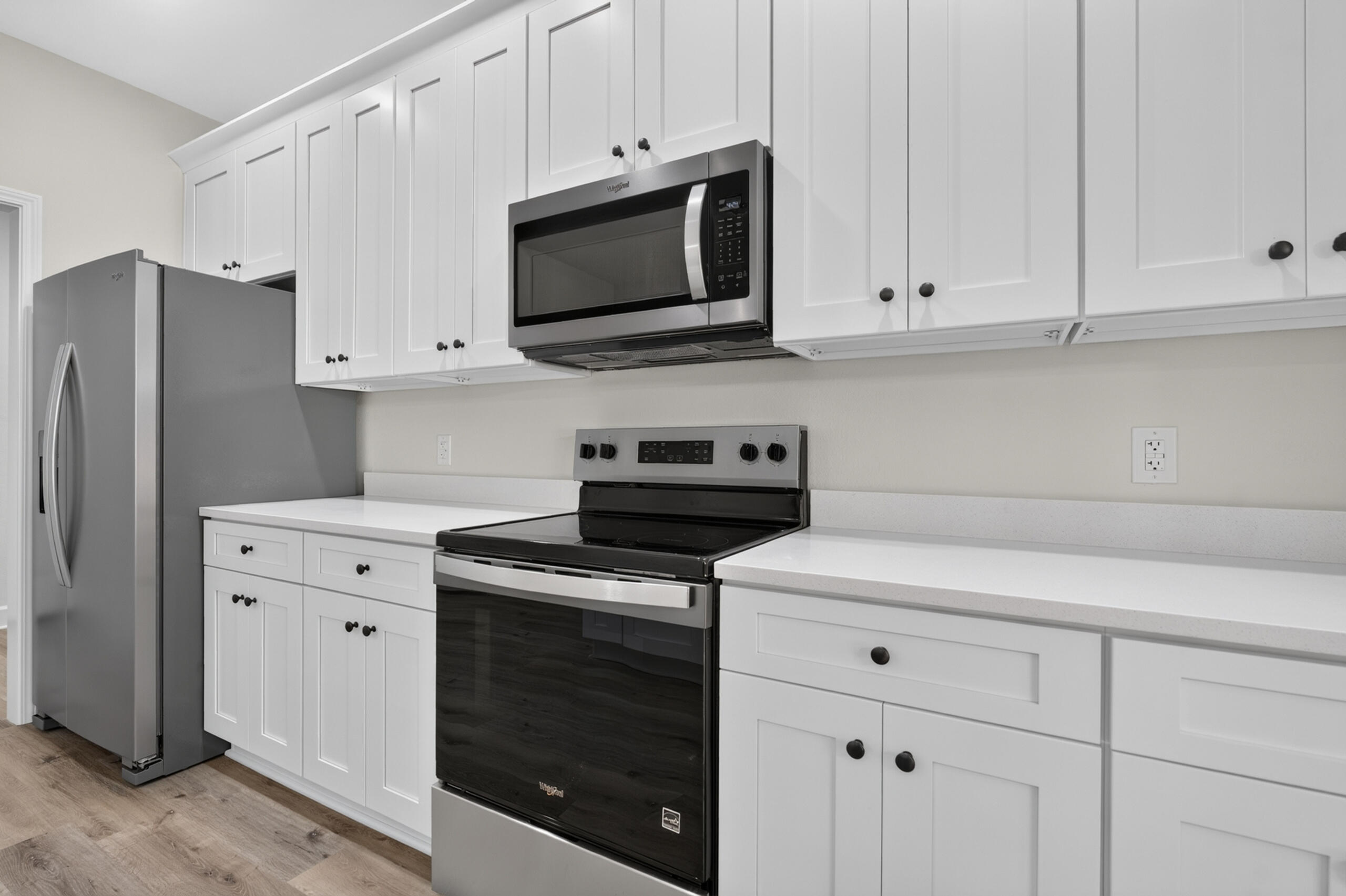 Kitchen with white cabinets, stainless refrigerator, and black glass range beneath a microwave.