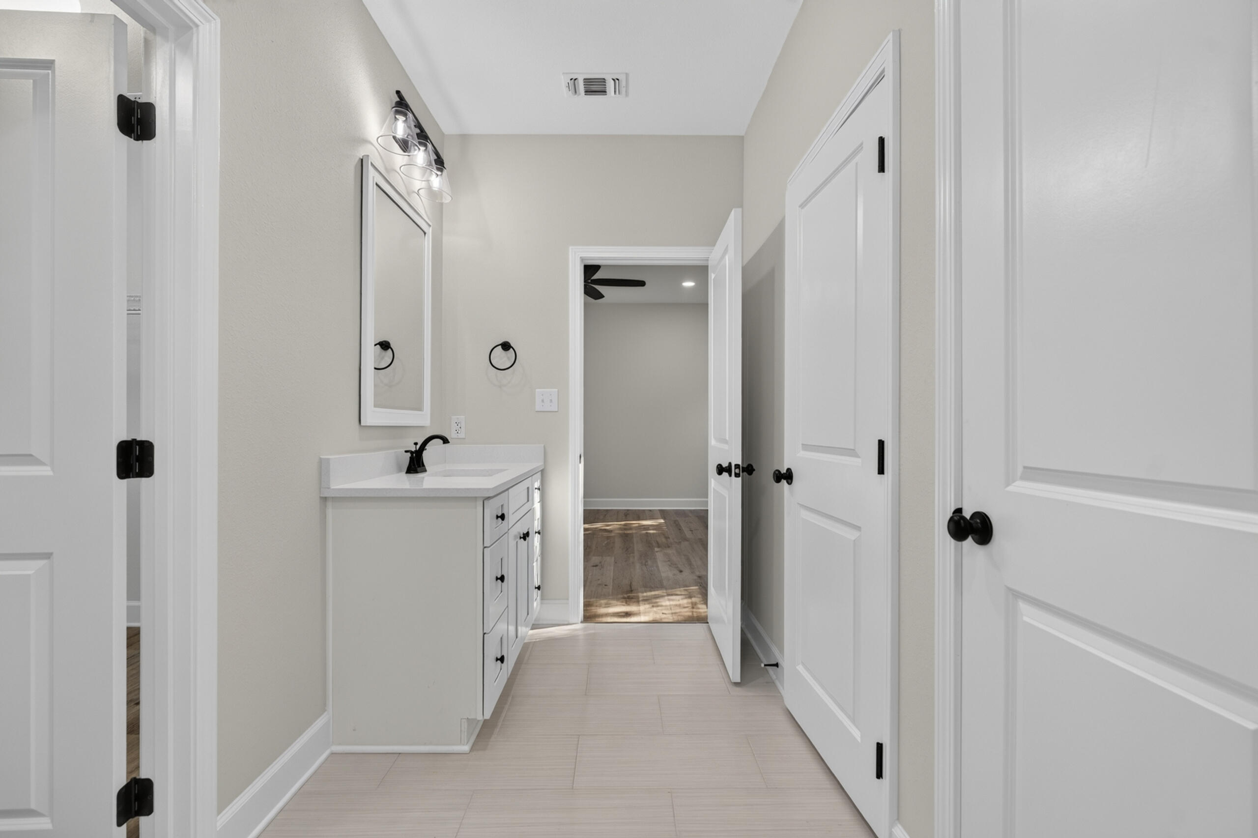 Bathroom vanity with a white countertop, black faucet, and open doors leading to a wood-floored room.