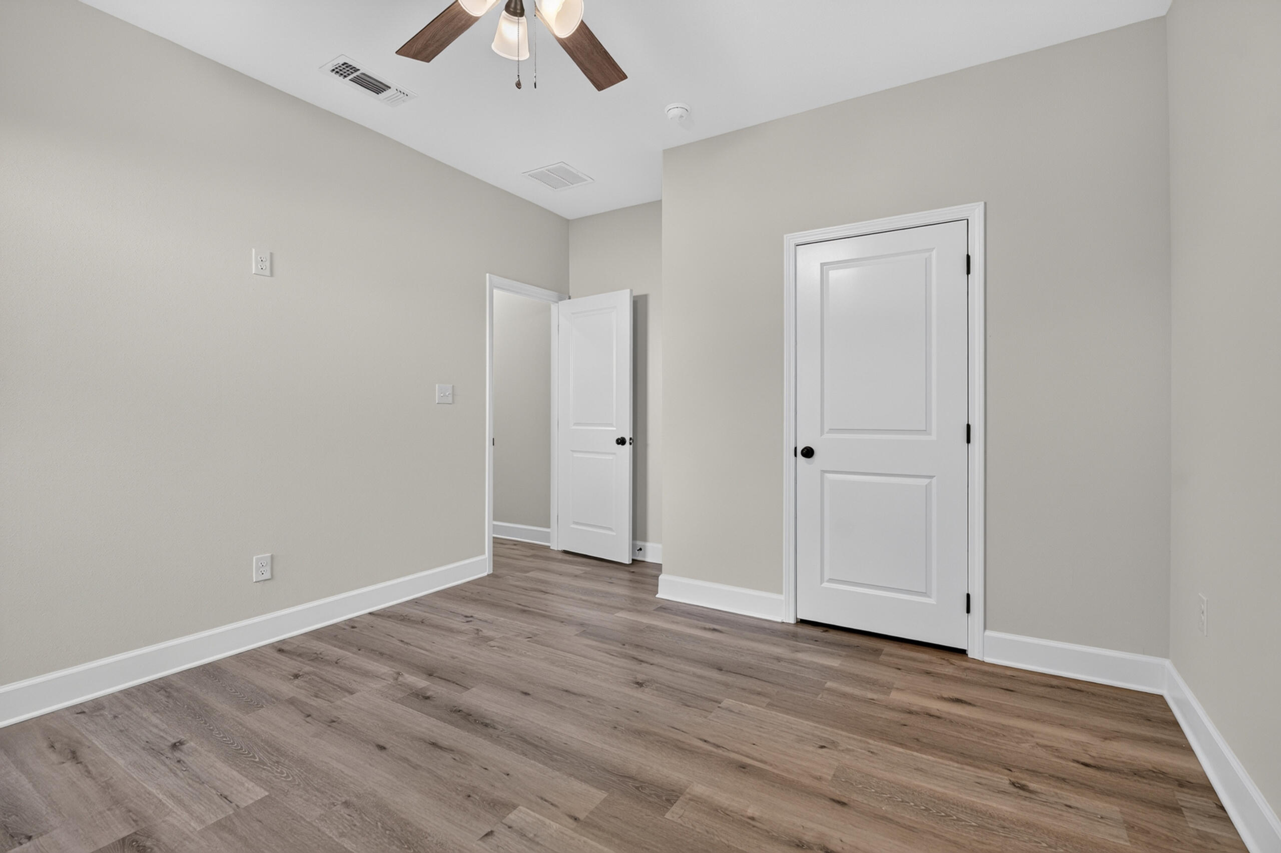 Empty room with wood-look flooring, two white paneled doors, and a ceiling fan.