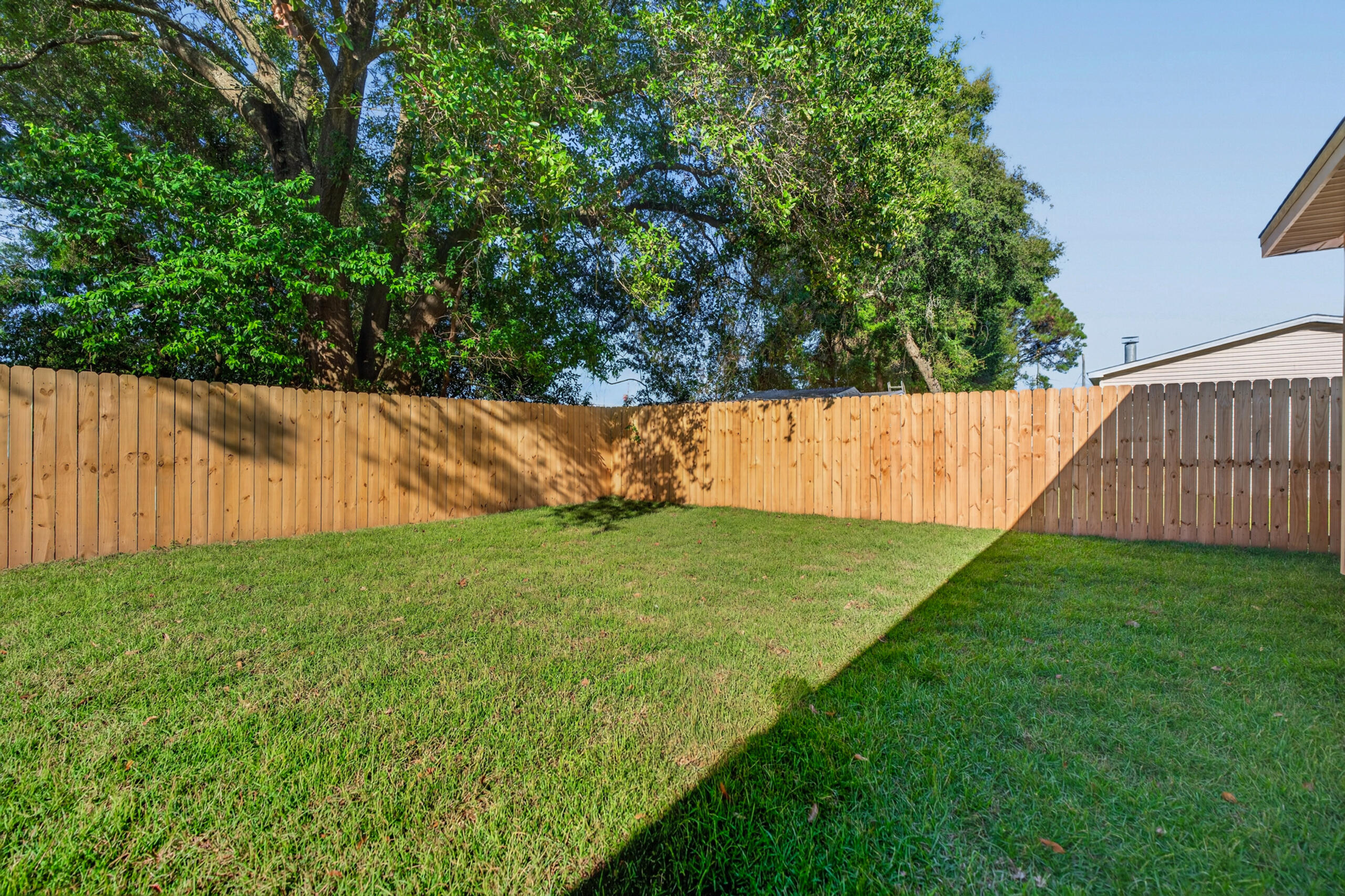 Fenced backyard with a green lawn, wooden privacy fence, and mature trees.