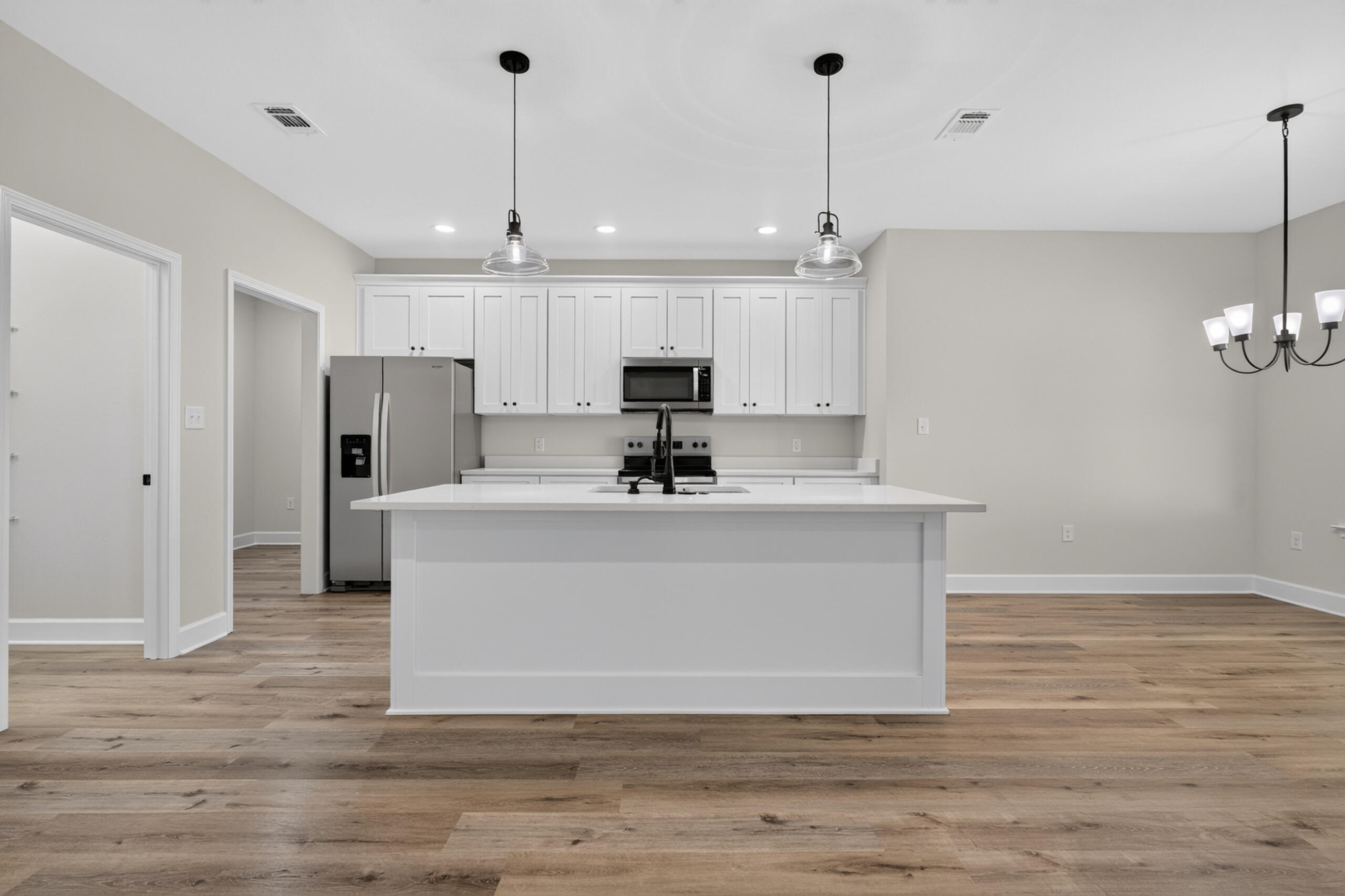 Vacant kitchen with a large white island, shaker cabinets, stainless steel appliances, and wood-look floors.