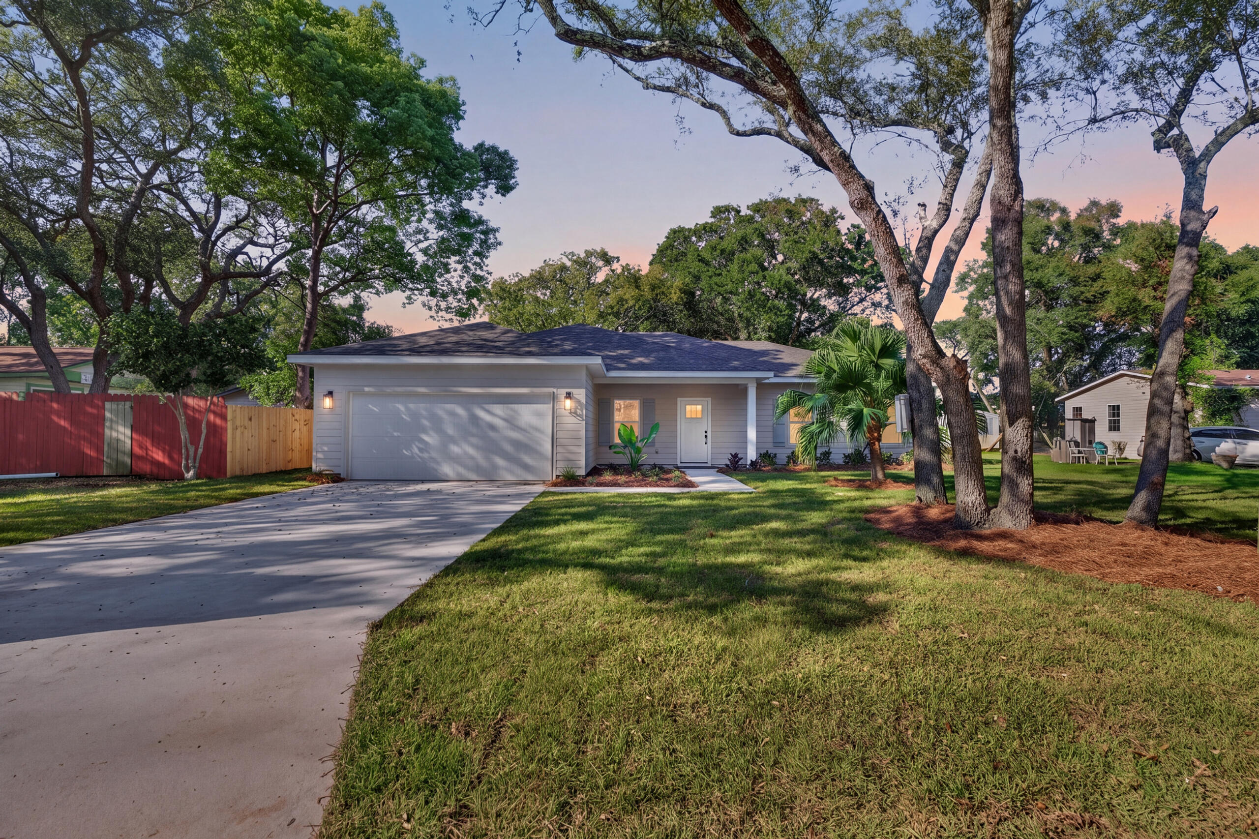 Single-story gray house with a two-car garage, broad driveway, and mature trees at dusk.