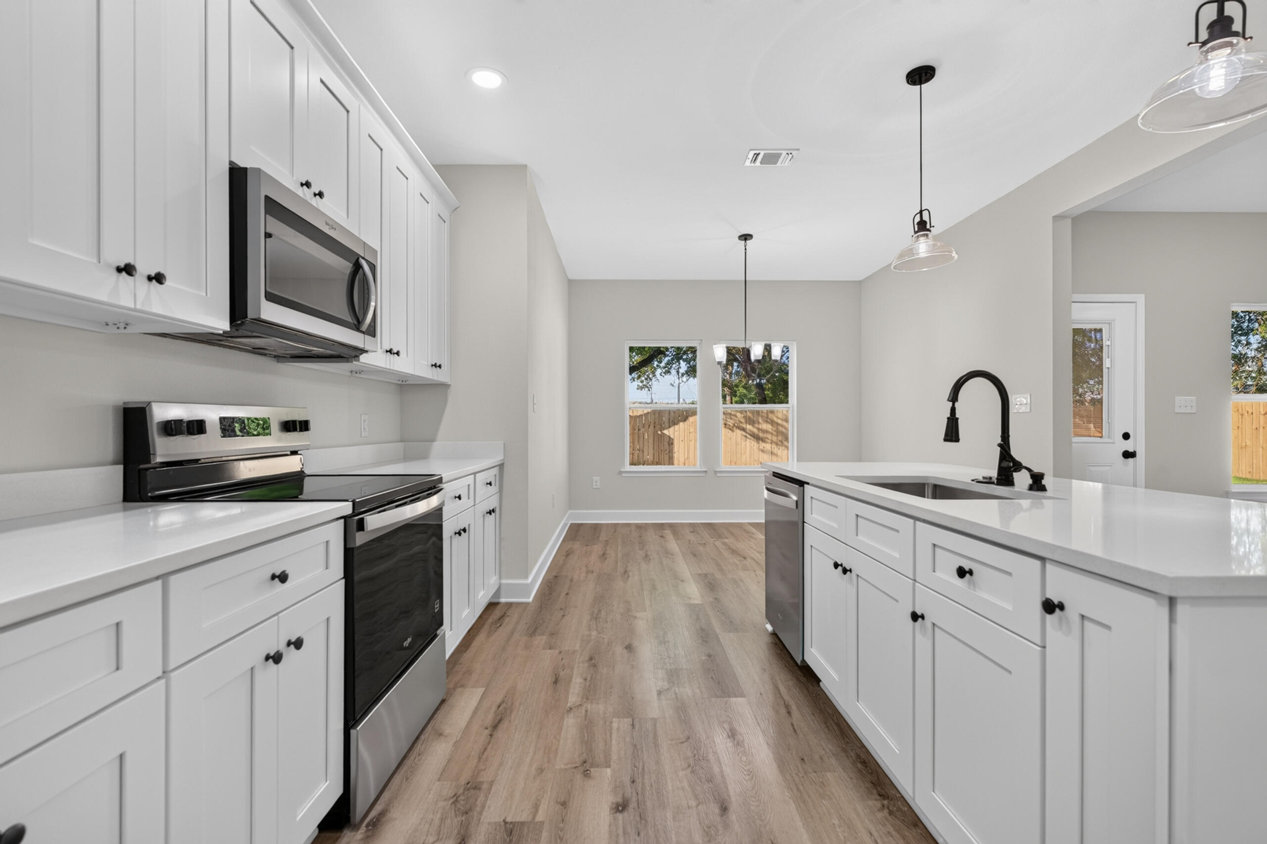 Bright kitchen with white cabinets, stainless steel appliances, a large island, and wood-look floors.