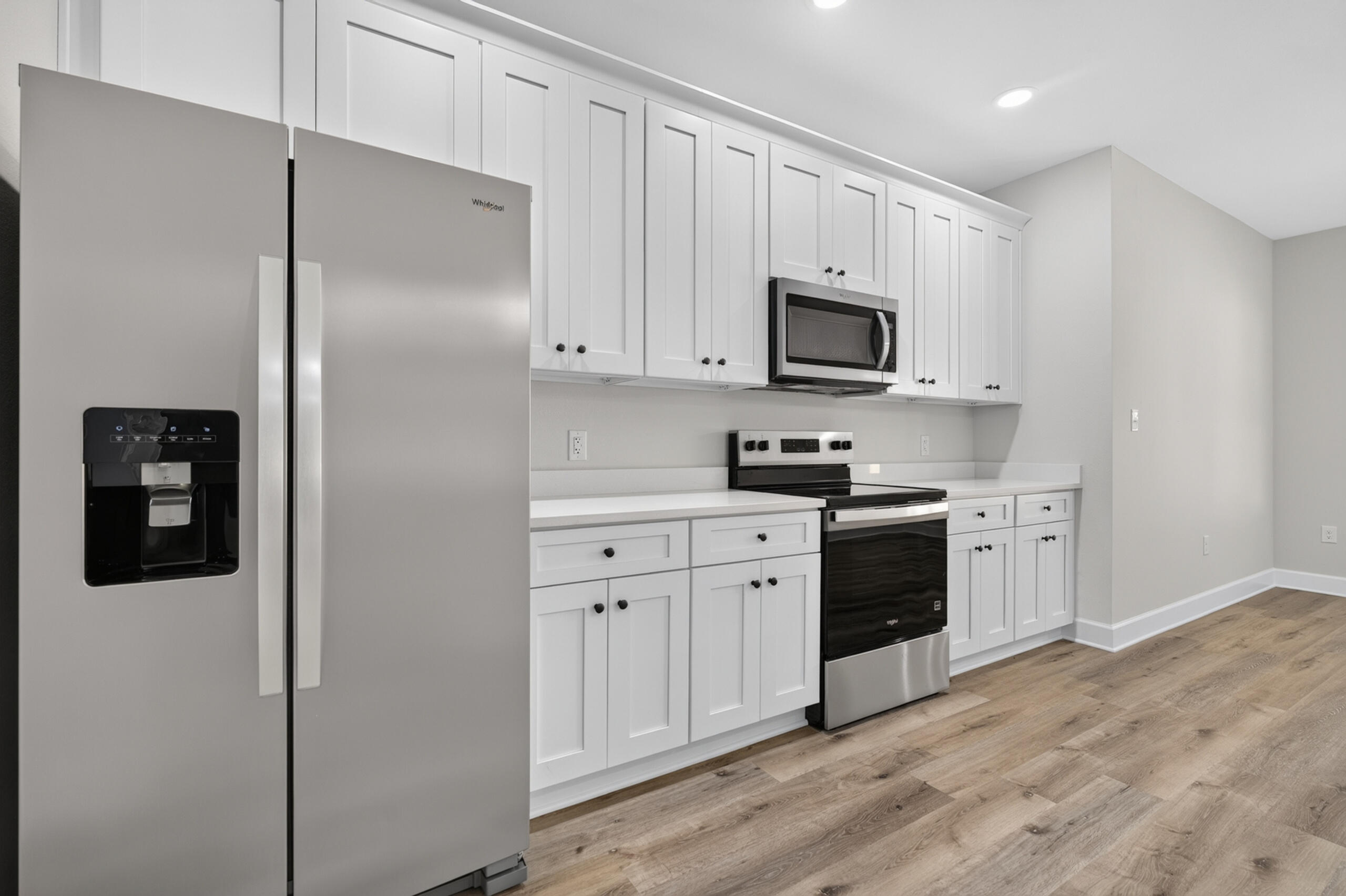 Kitchen with white shaker cabinets, stainless steel appliances, and light wood-look flooring.