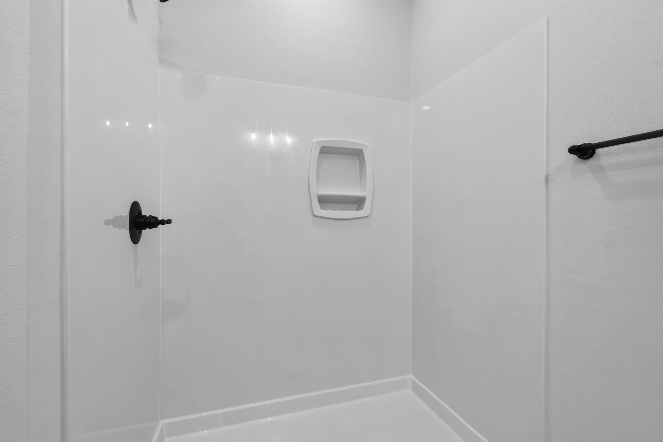 White shower stall with a built-in shelf, black shower control, and grab bar.