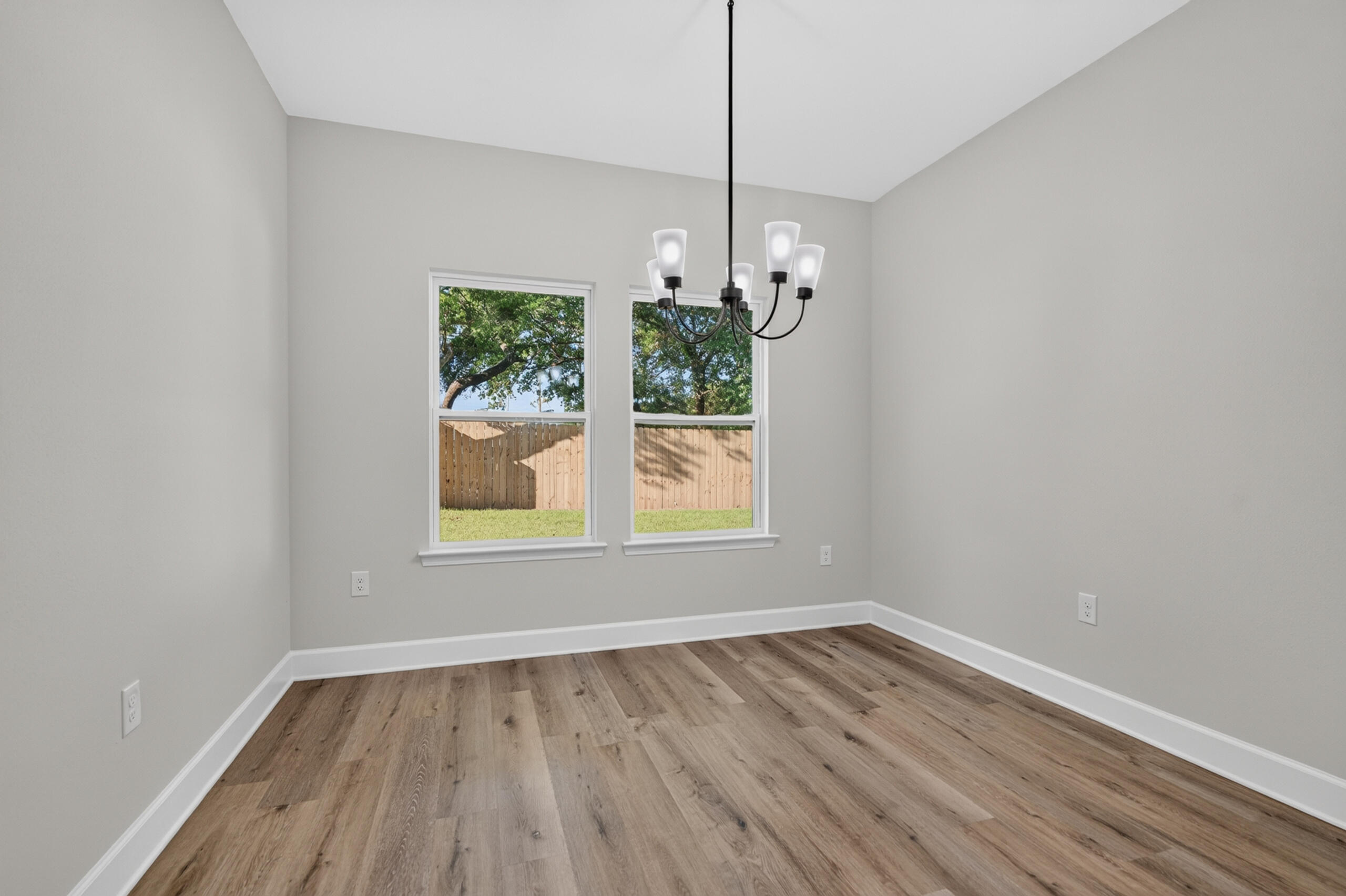 Empty dining room with wood-look flooring, two yard-facing windows, and a chandelier.