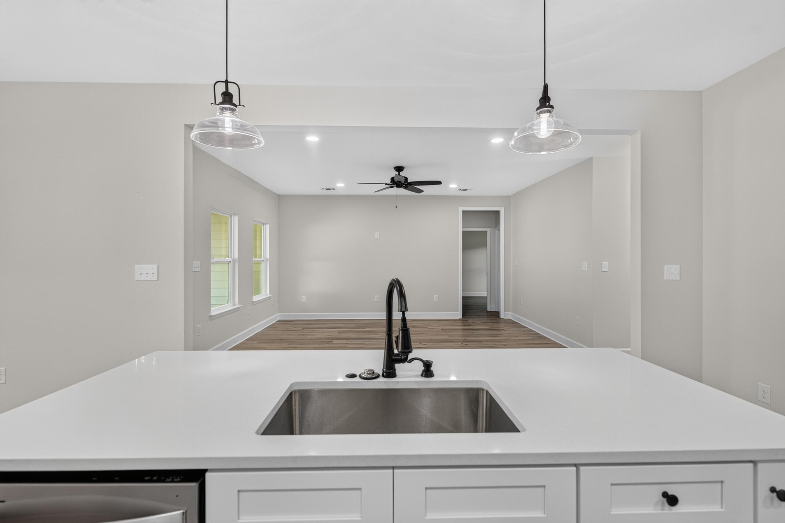 Vacant kitchen with a white island, stainless steel sink, and glass pendant lights facing an open room.