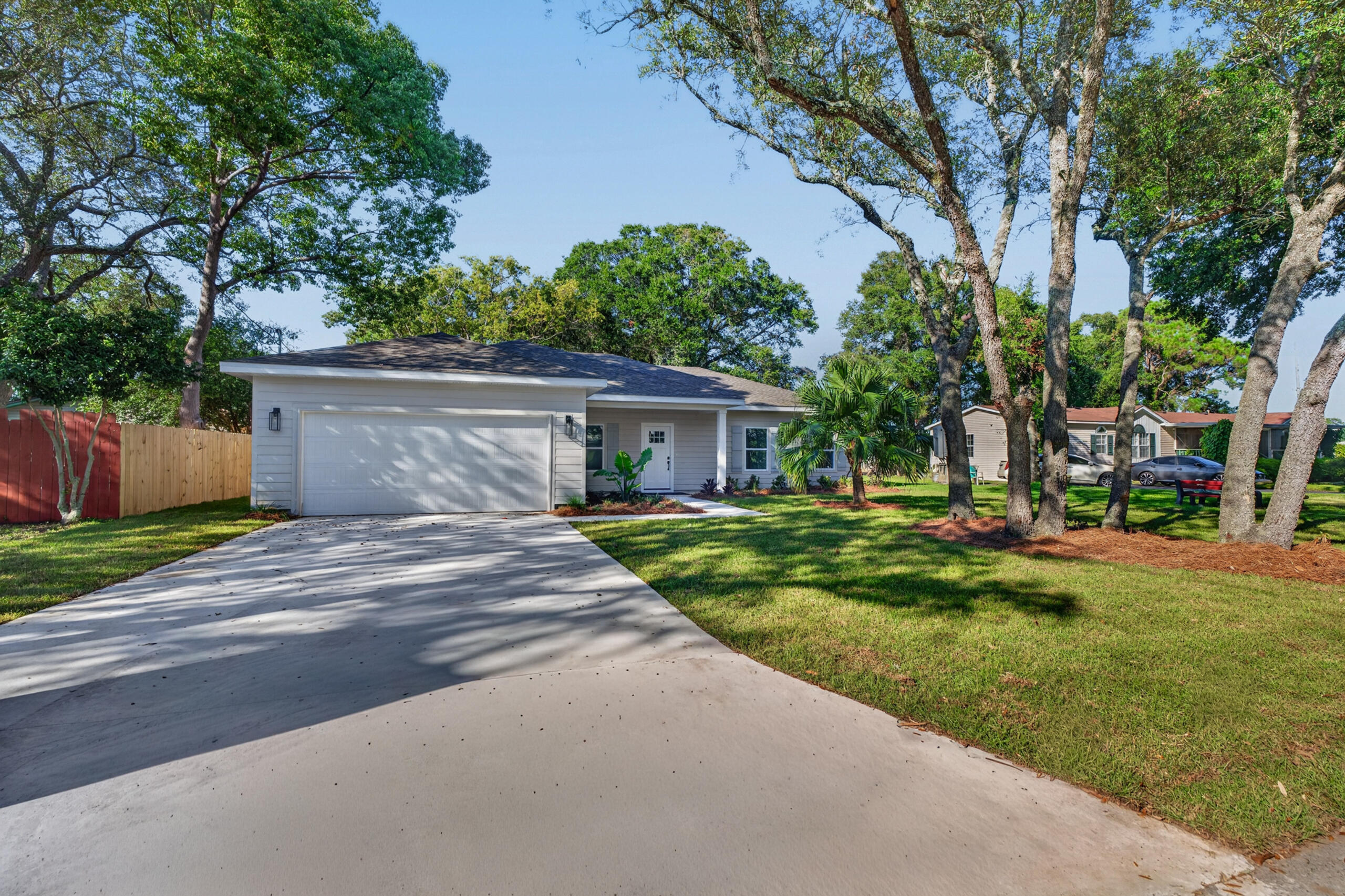 Light gray single-story home with an attached garage, broad driveway, and mature trees across the front lawn.