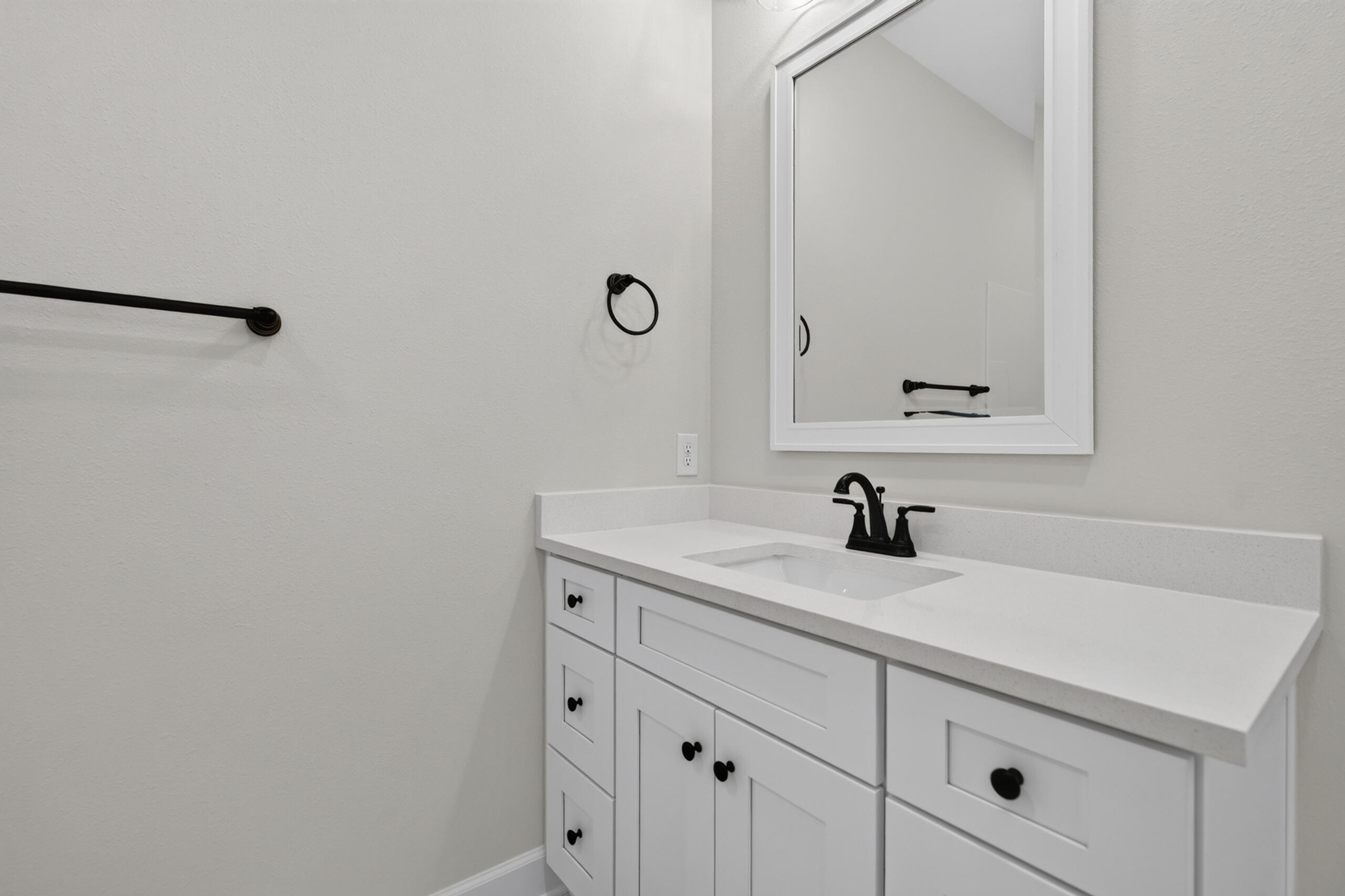 Bathroom vanity with a white cabinet, black faucet and hardware, and a large framed mirror.