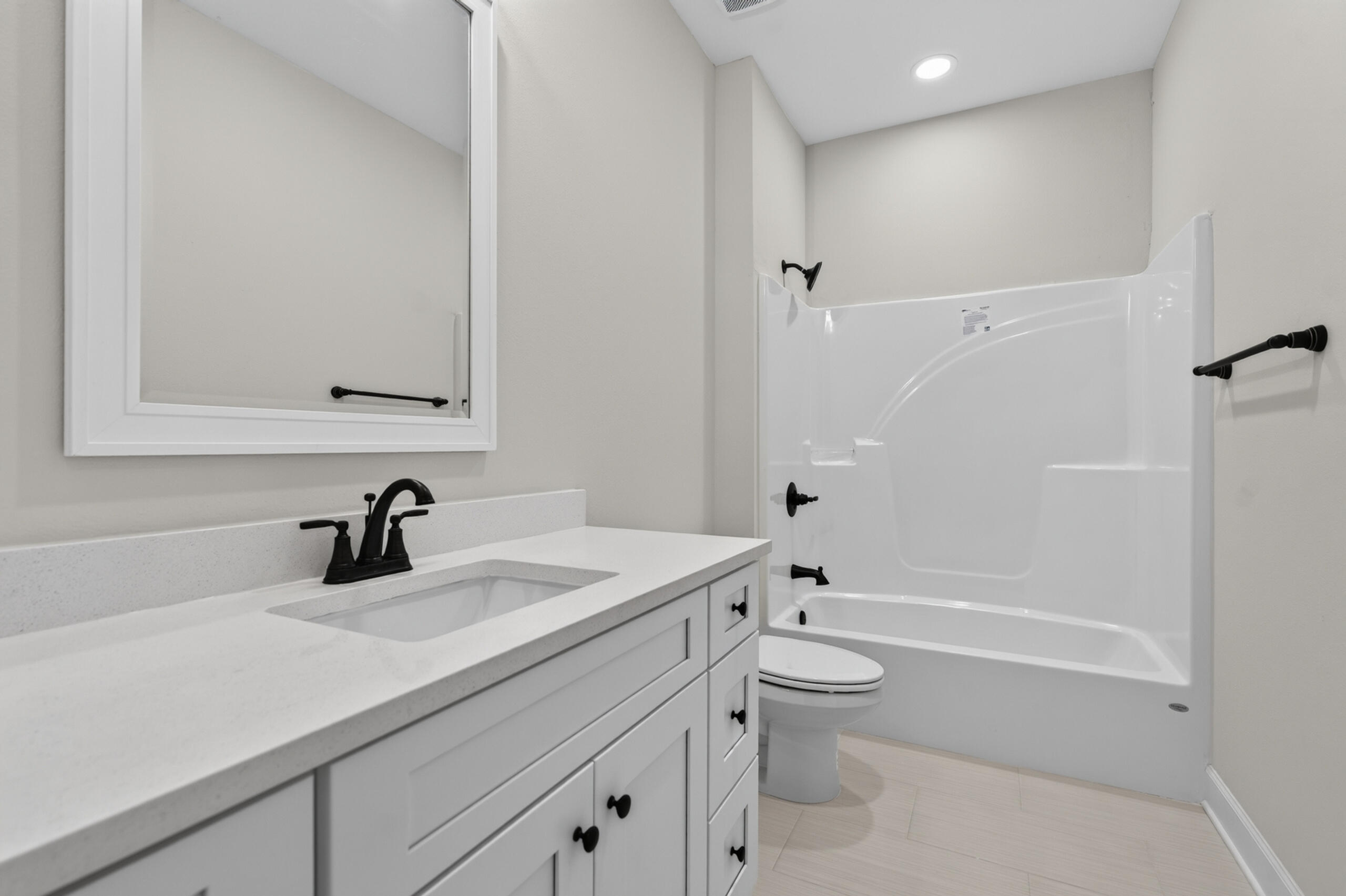 Bathroom with a white vanity, framed mirror, toilet, and tub-shower with black fixtures.