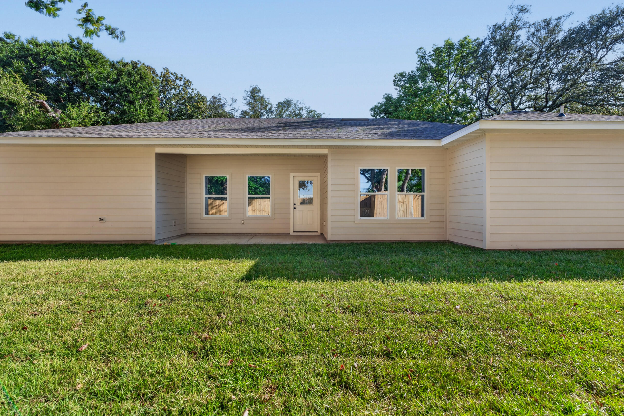 Single-story beige house with a covered rear entry and broad green lawn.