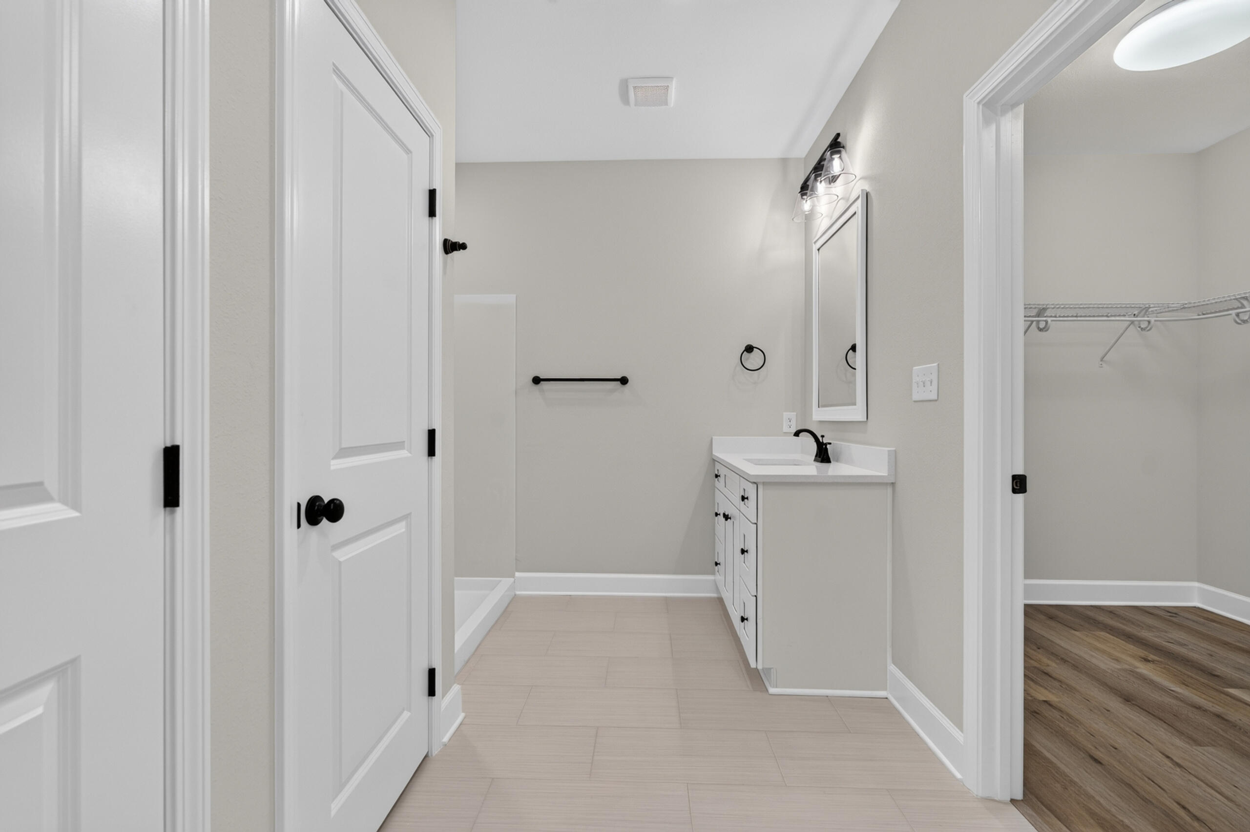 Vacant bathroom with white vanity, black fixtures, pale tile floor, and doorway to a walk-in closet.