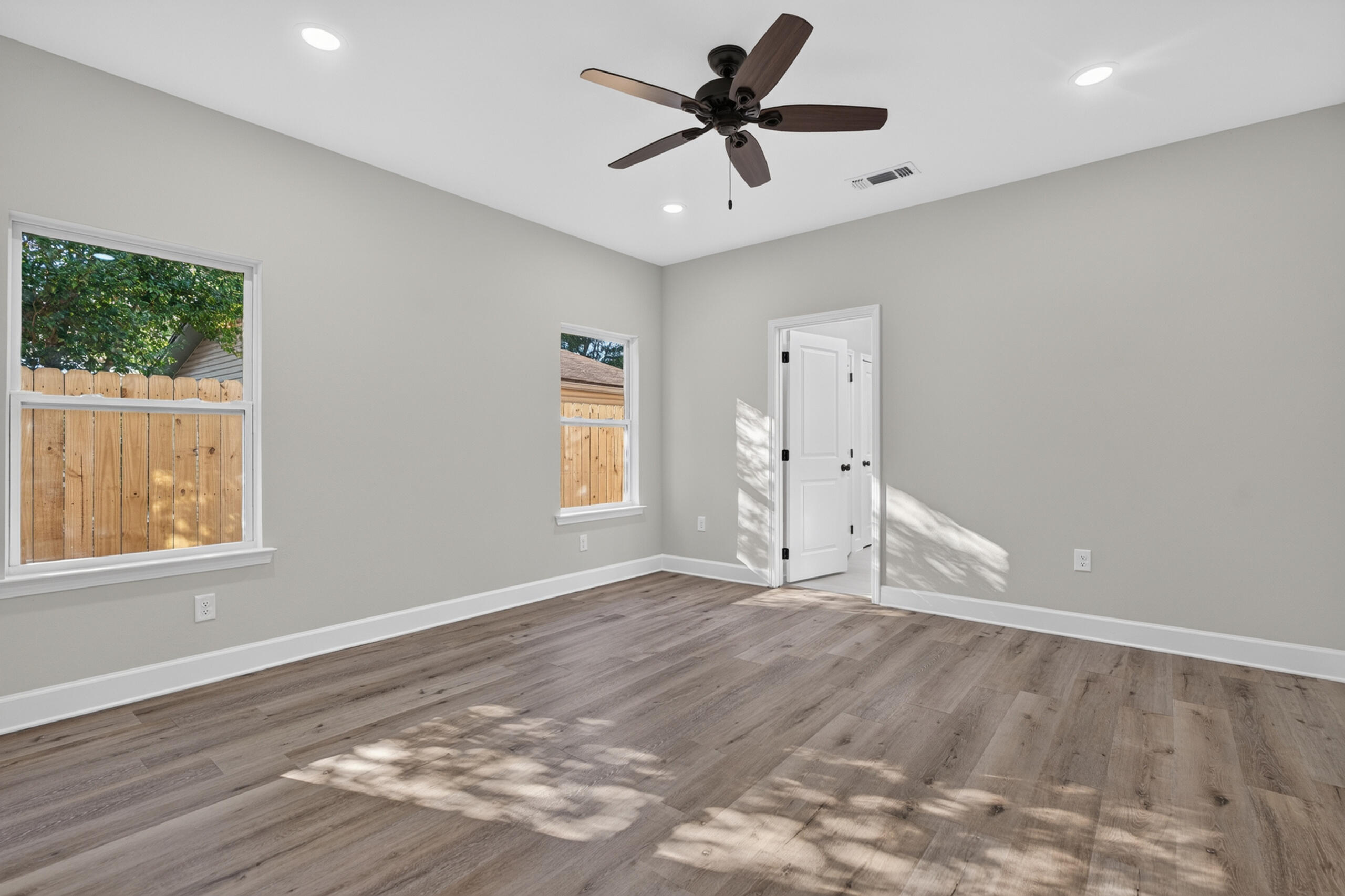 Empty room with wood-look flooring, two windows, and a dark ceiling fan.
