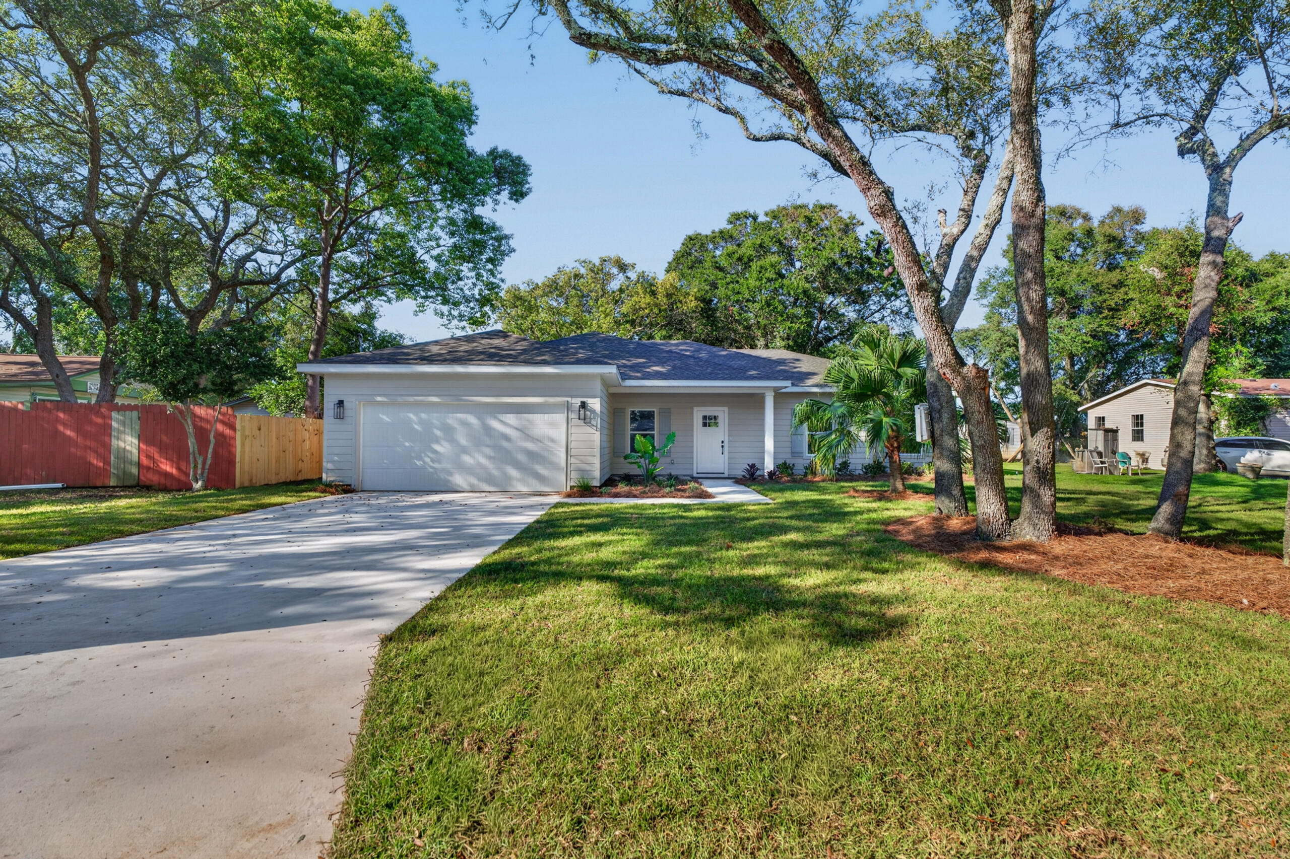 Single-story home with an attached garage, wide driveway, and mature trees across the front lawn.
