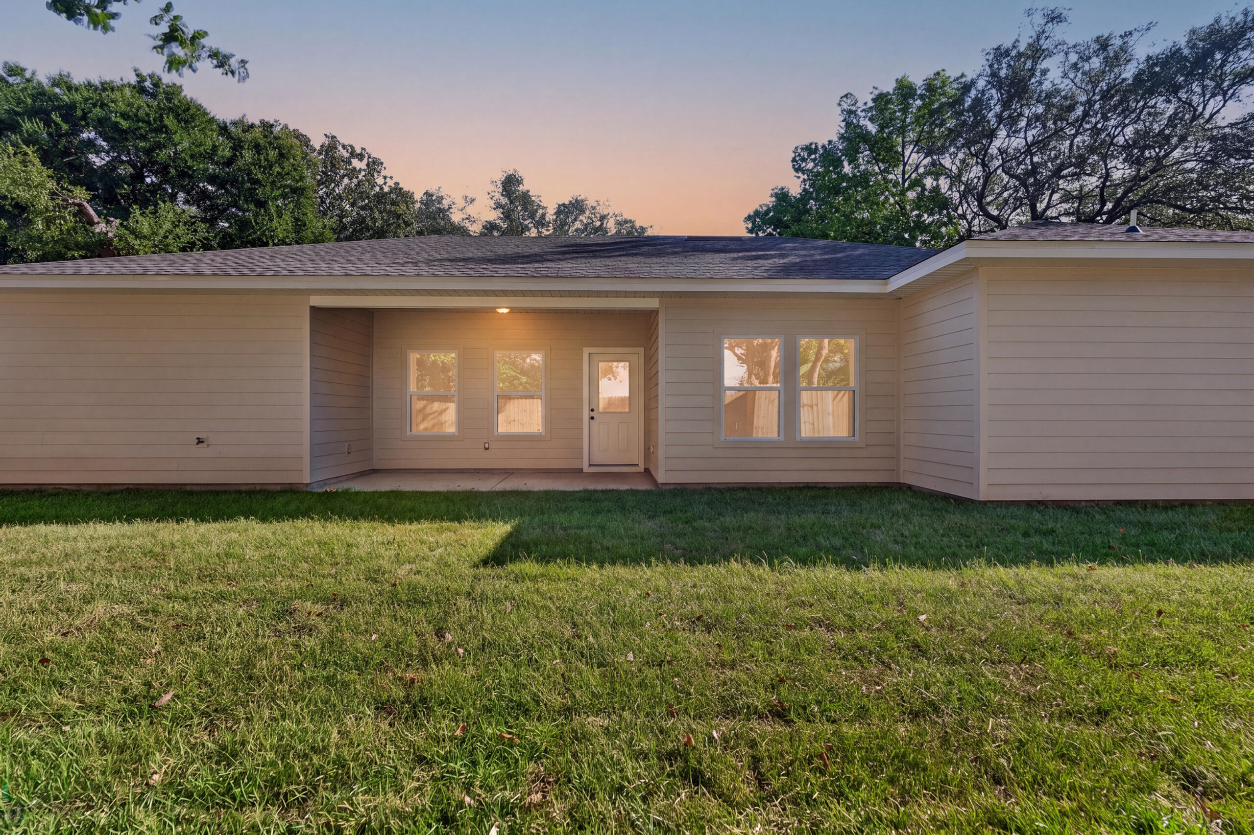 Single-story home with a recessed covered entry and broad green lawn in warm evening light.