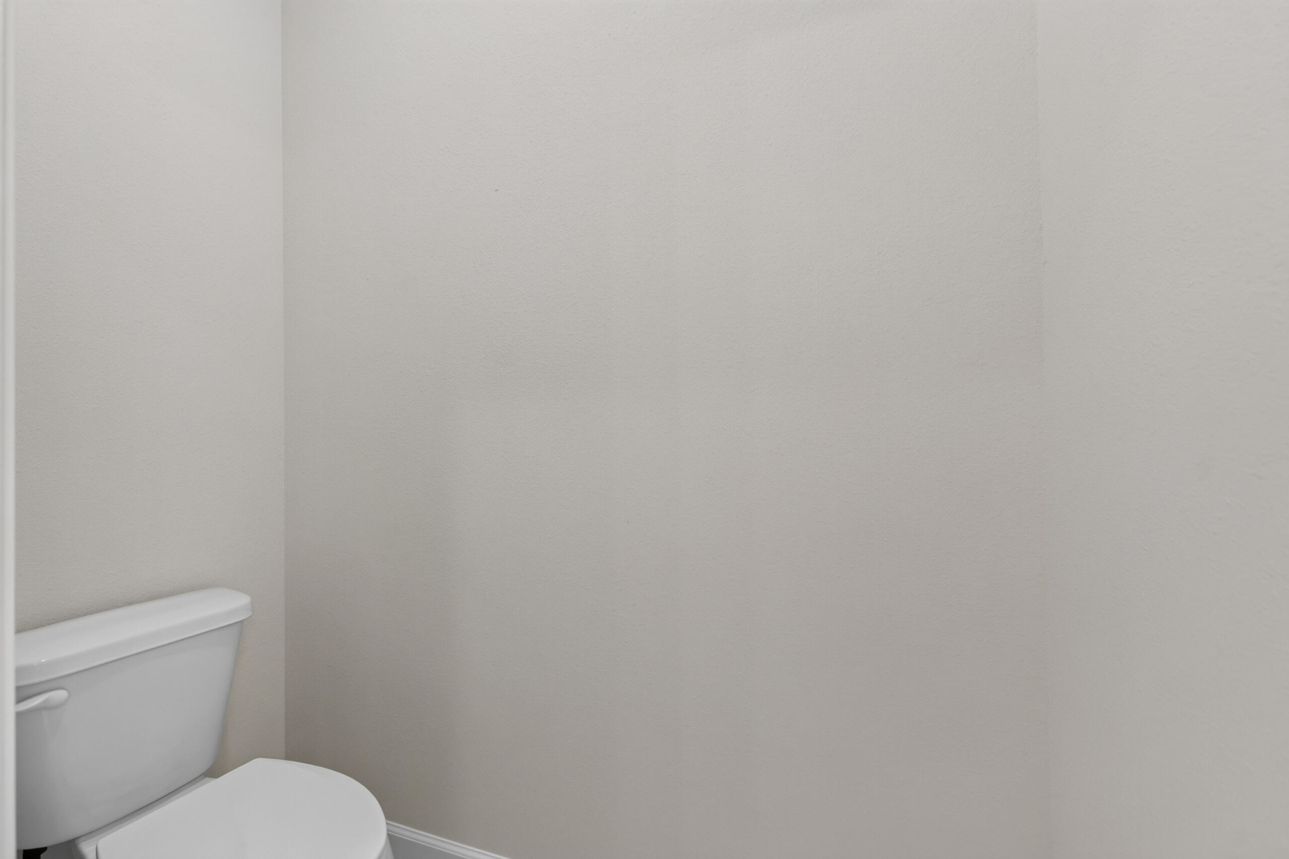 Bathroom with a white toilet and plain beige walls.