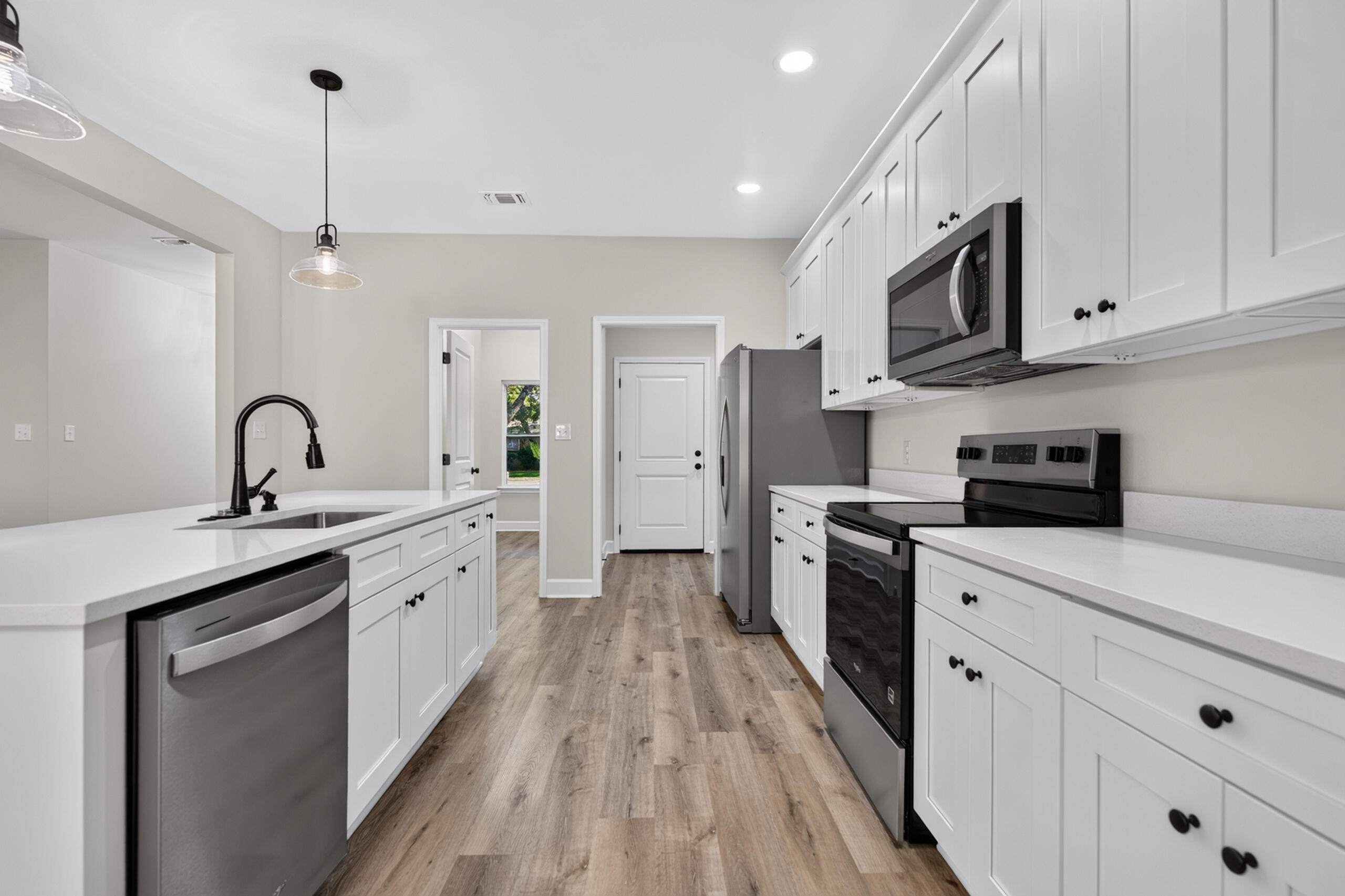 Kitchen with white cabinets, stainless steel appliances, and wood-look plank flooring.