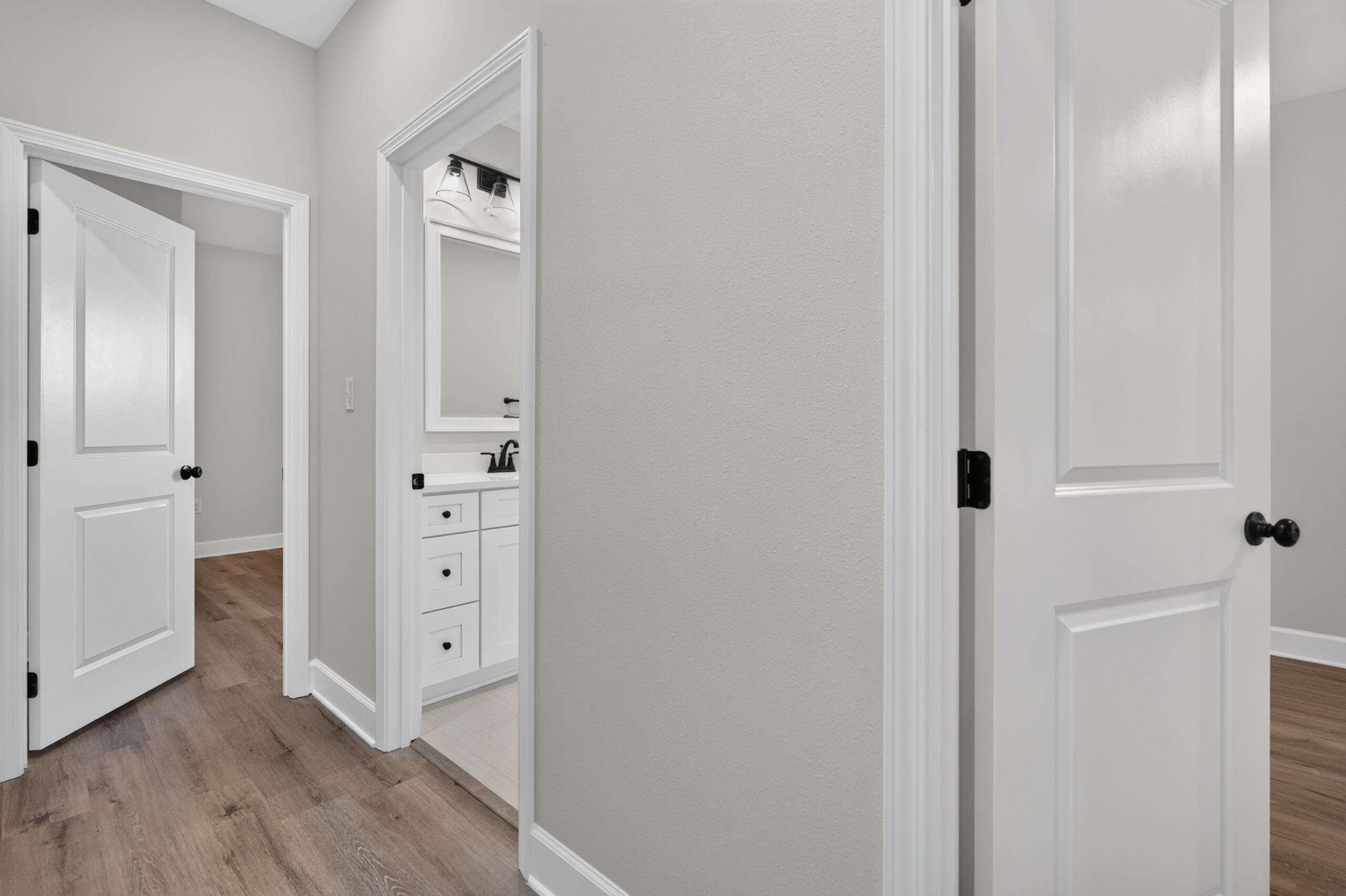 Hallway with wood-look flooring and an open doorway revealing a white bathroom vanity.