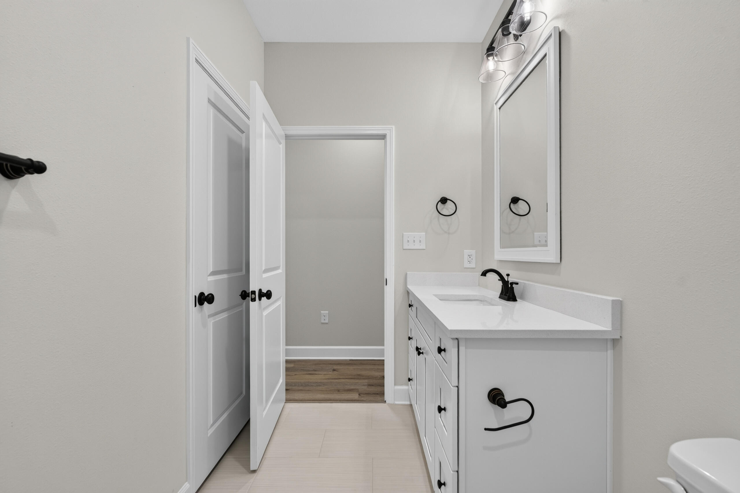 Bathroom with a long white vanity, black faucet and hardware, framed mirror, and open doorway.