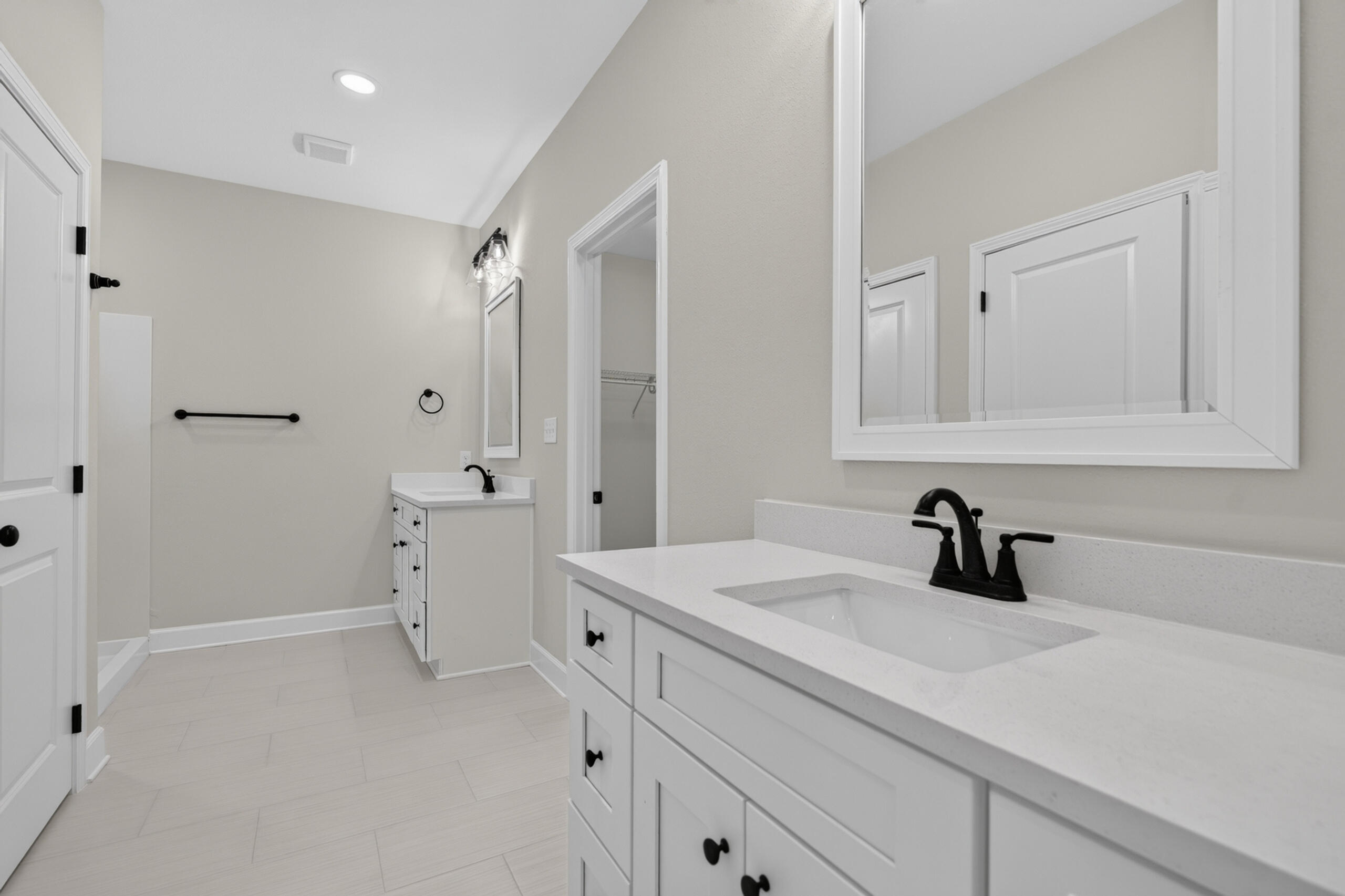 Bathroom with two white vanities, a large mirror, and black fixtures.