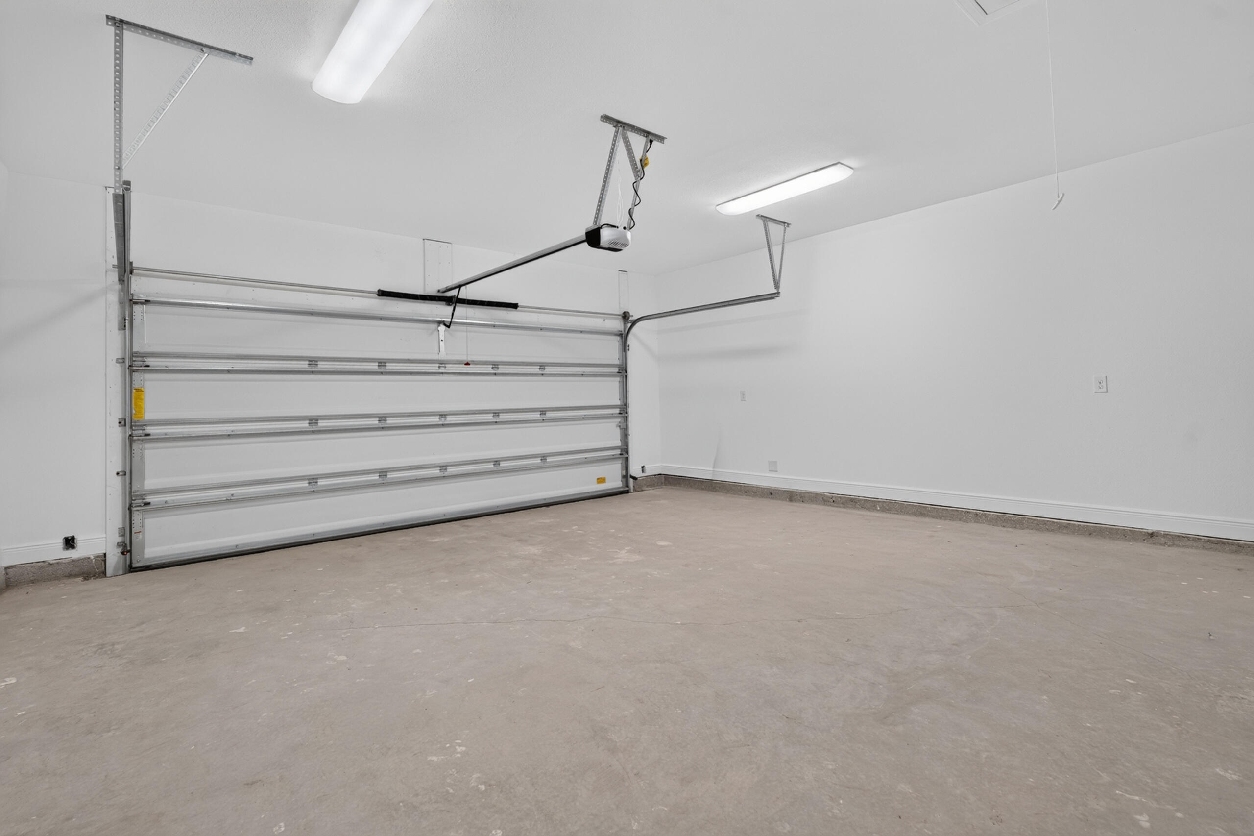 Empty garage with a wide sectional door and bare concrete floor.