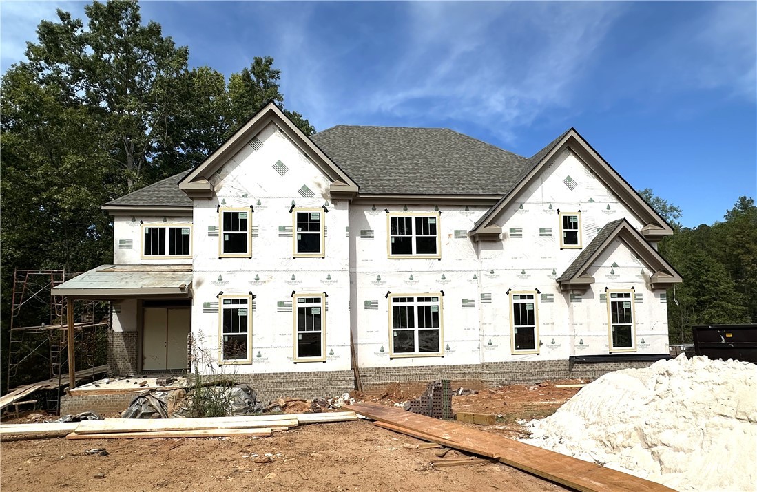 Two-story house under construction with multiple gables, white building wrap, and a brick foundation.