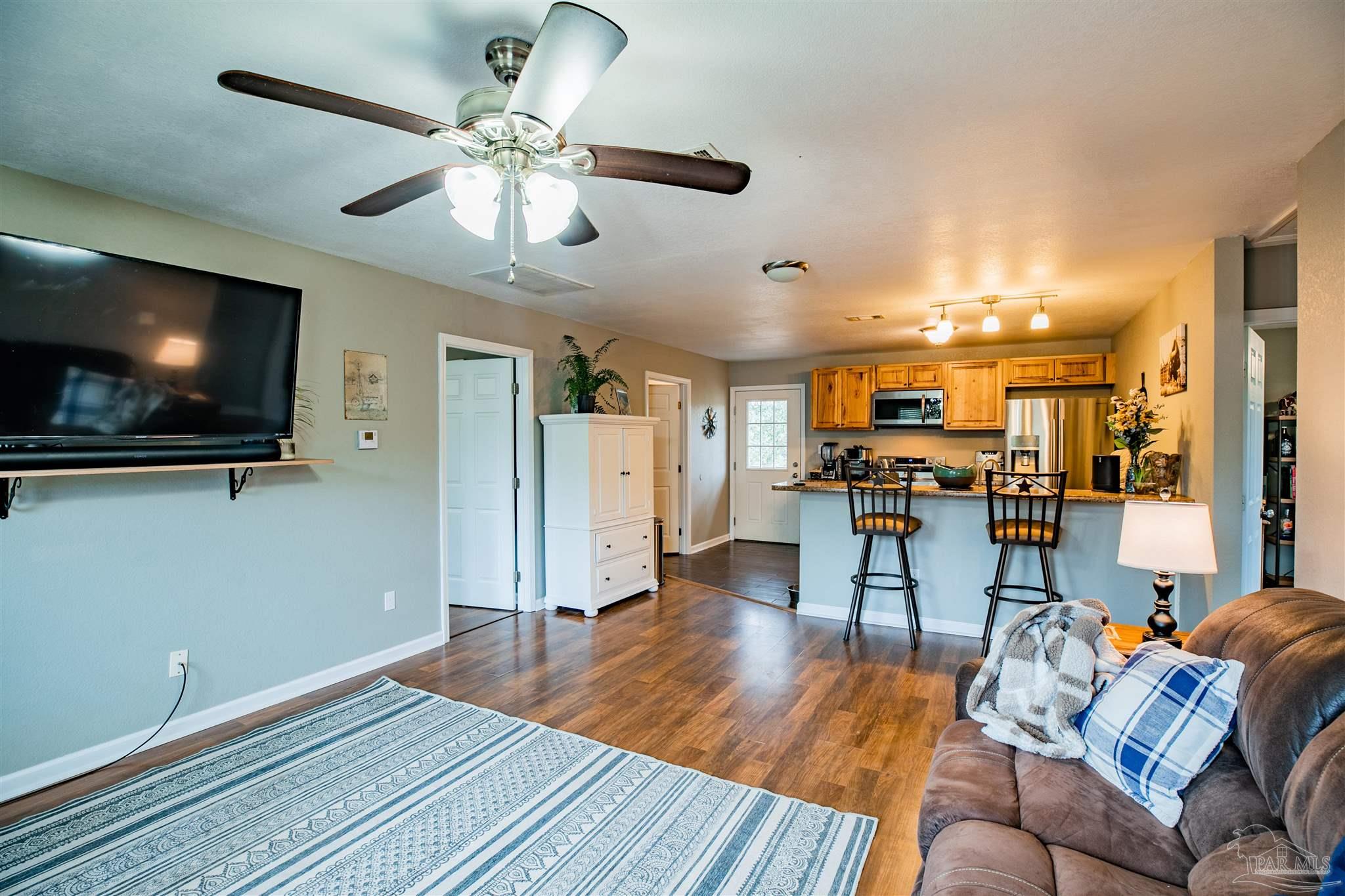 Open-plan living room and kitchen with a patterned rug, sofa, breakfast bar, and honey-colored cabinets.