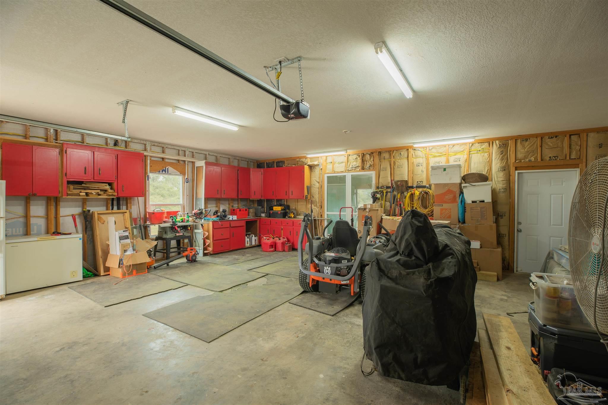 Garage workshop with red cabinets, workbenches, and a riding mower.