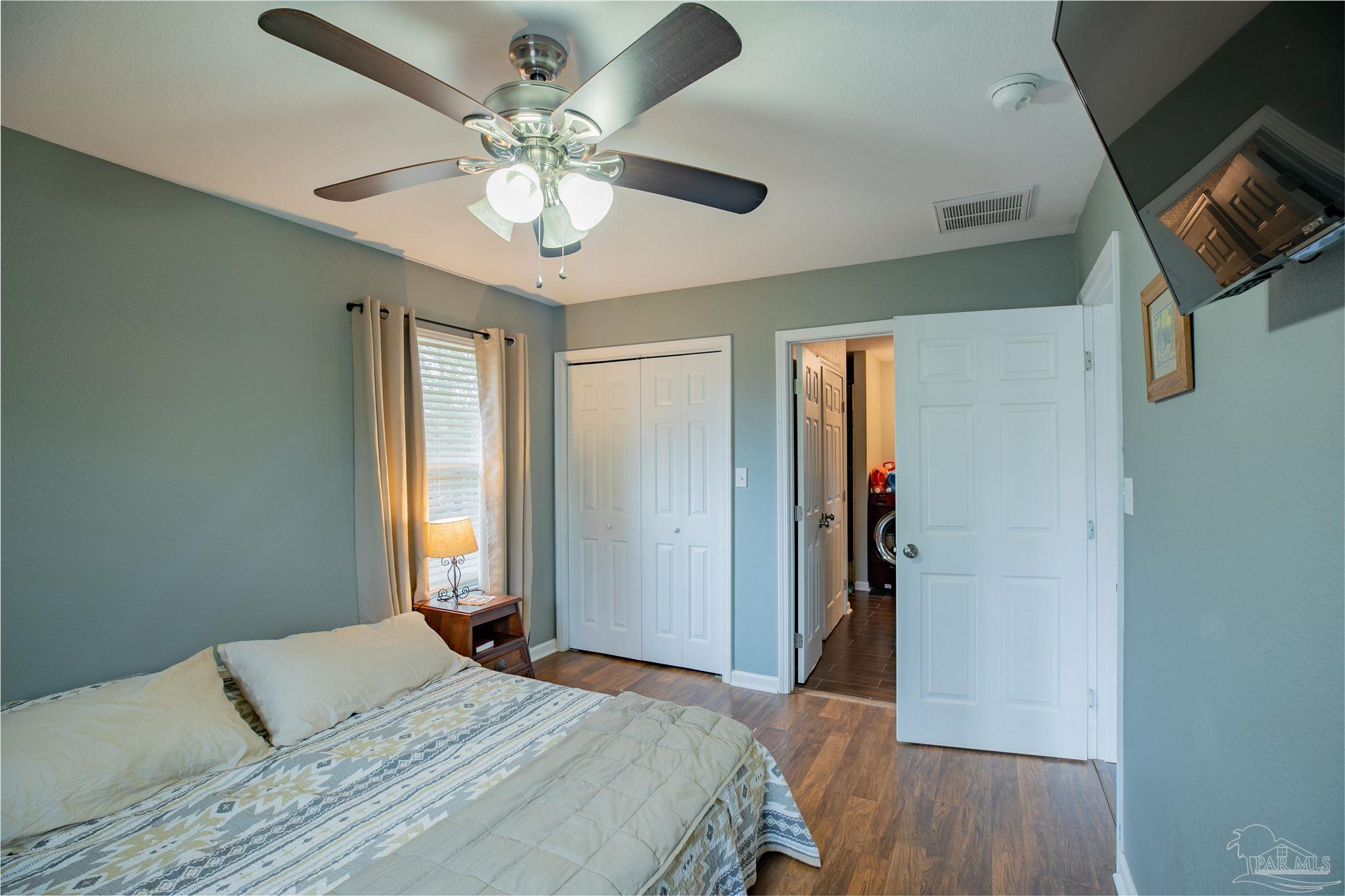 Furnished bedroom with a ceiling fan, wood-look floor, and open doorway to a laundry area.