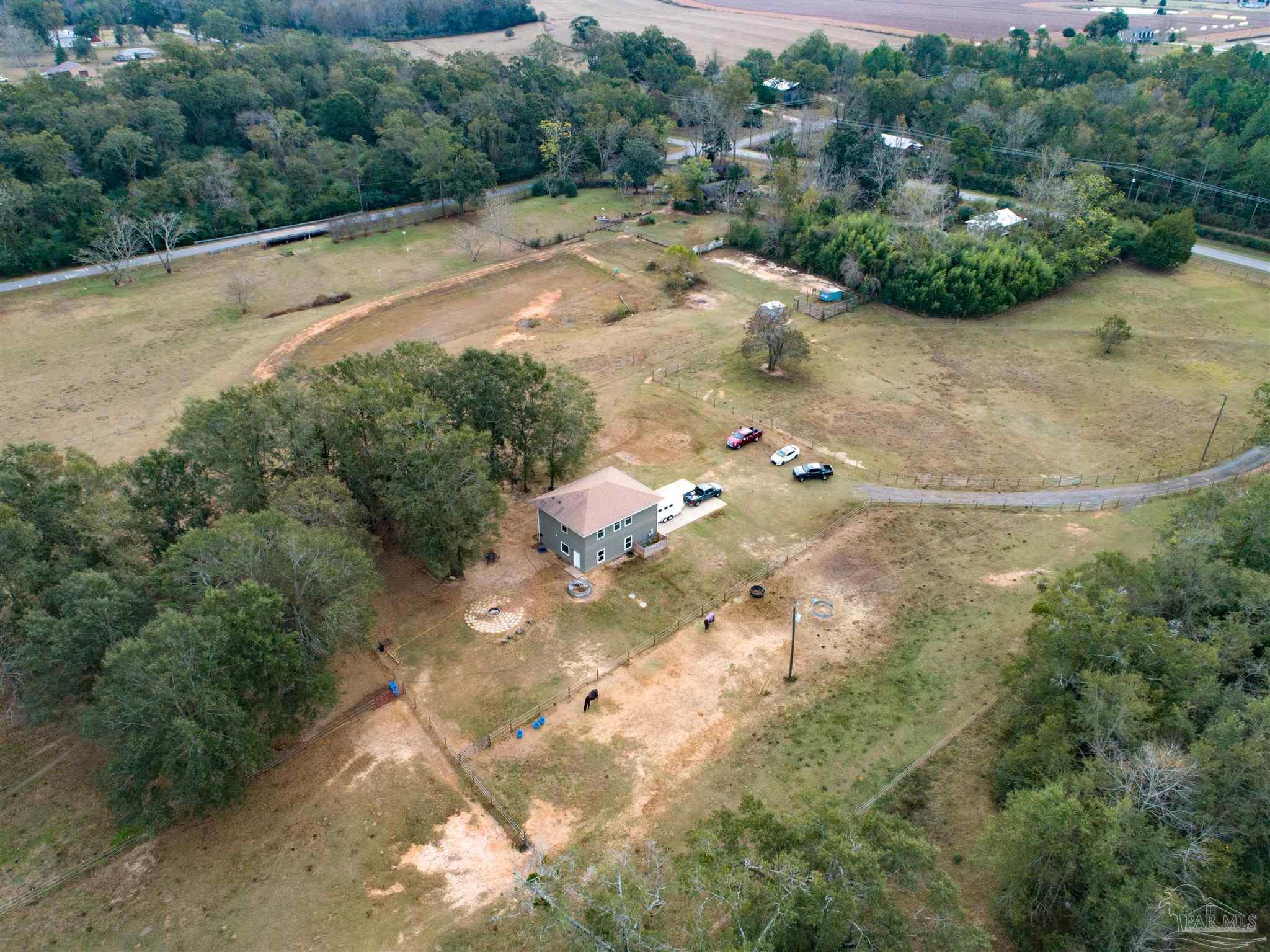 Aerial view of a gray two-story house on fenced acreage with horses and mature trees.