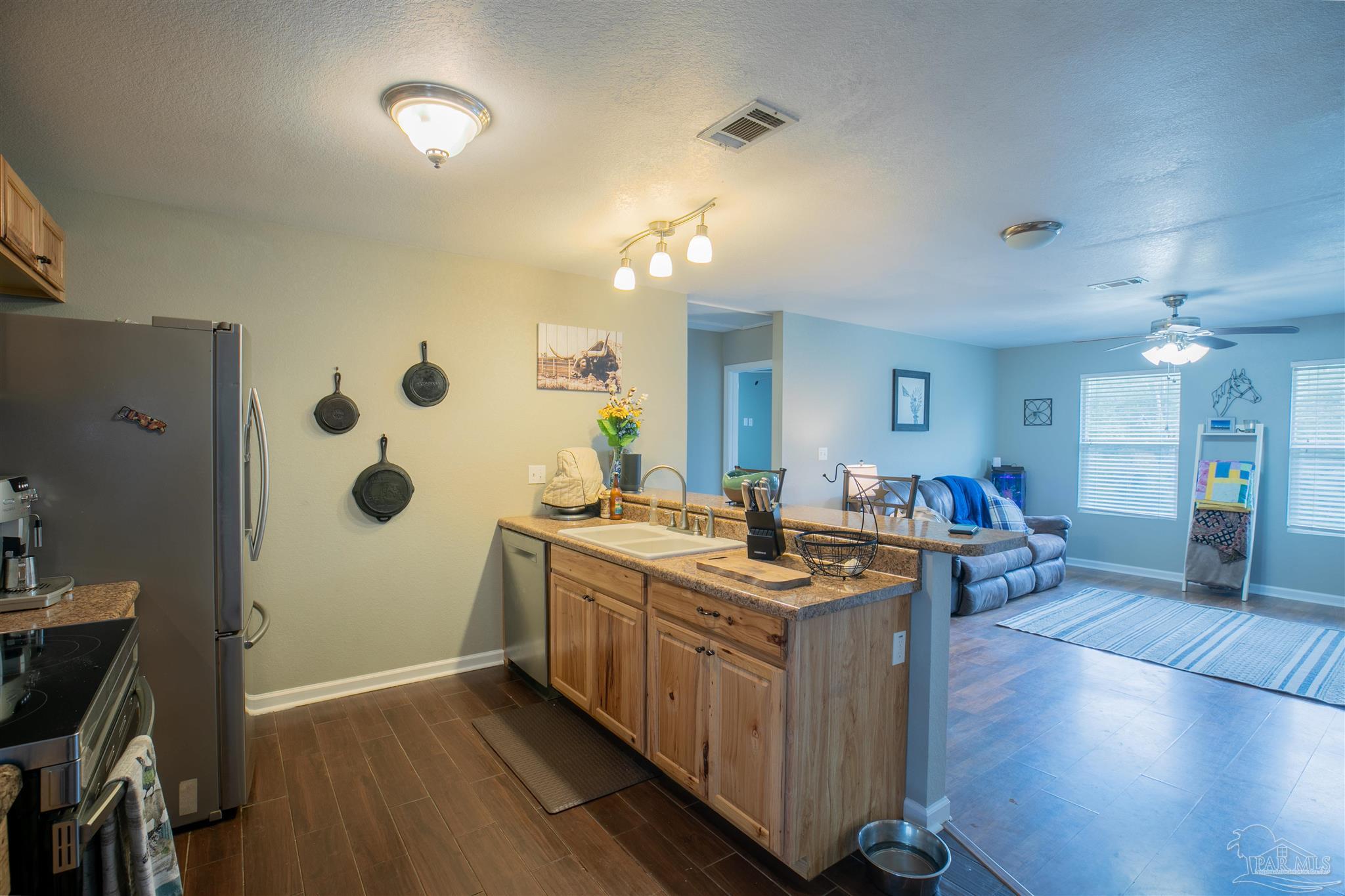 Kitchen with wood cabinets and granite counters opening into a living room with a blue sofa.