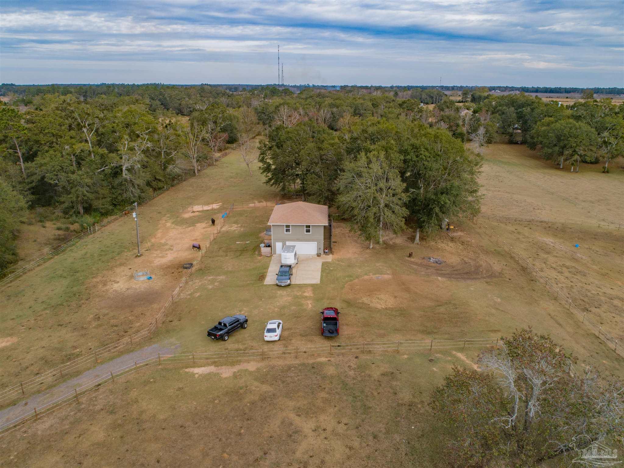 Aerial view of a rural home with fenced pasture, horses, and wooded surroundings.