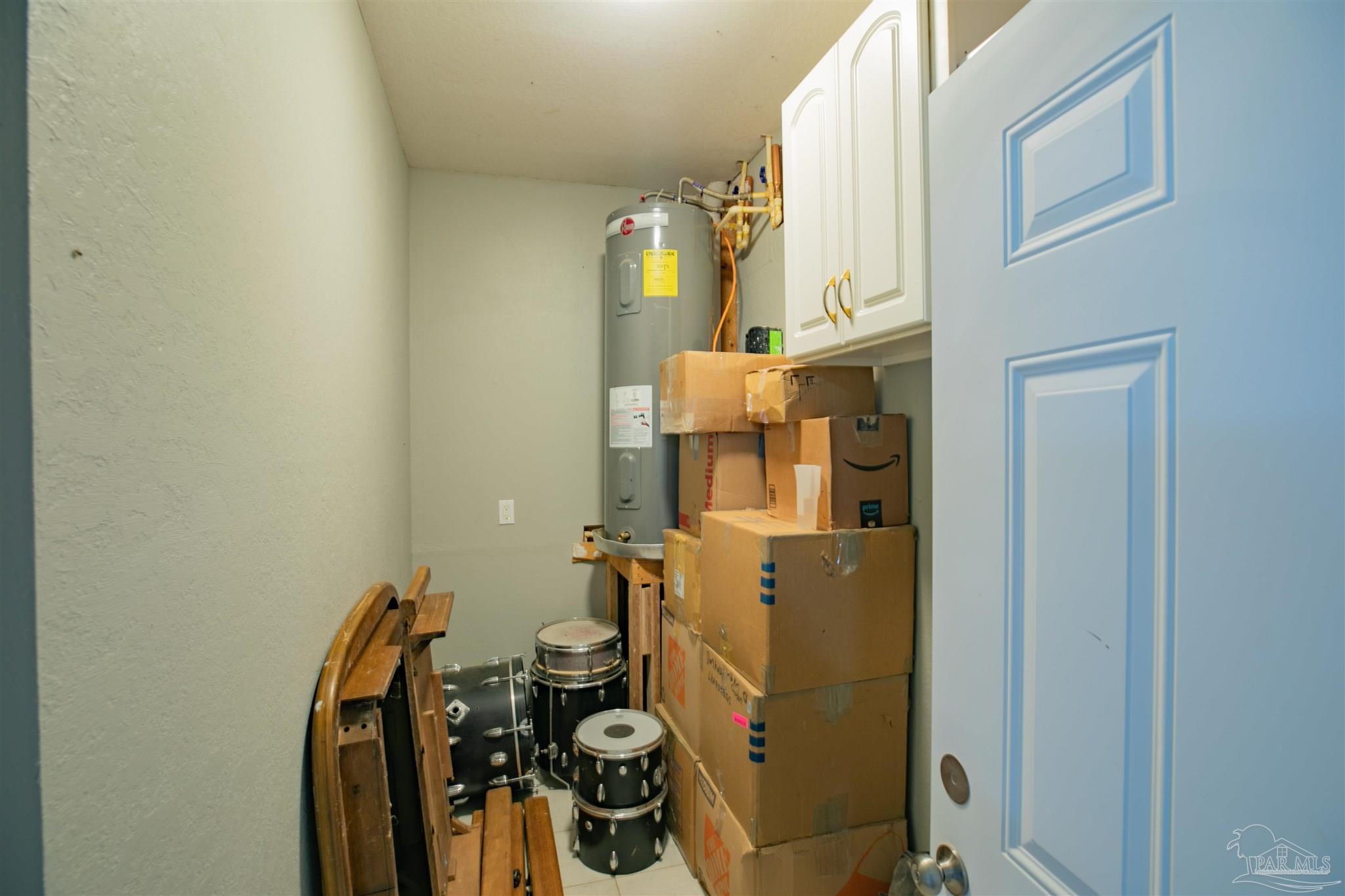 Utility room with a water heater, stacked boxes, and a stored drum set.