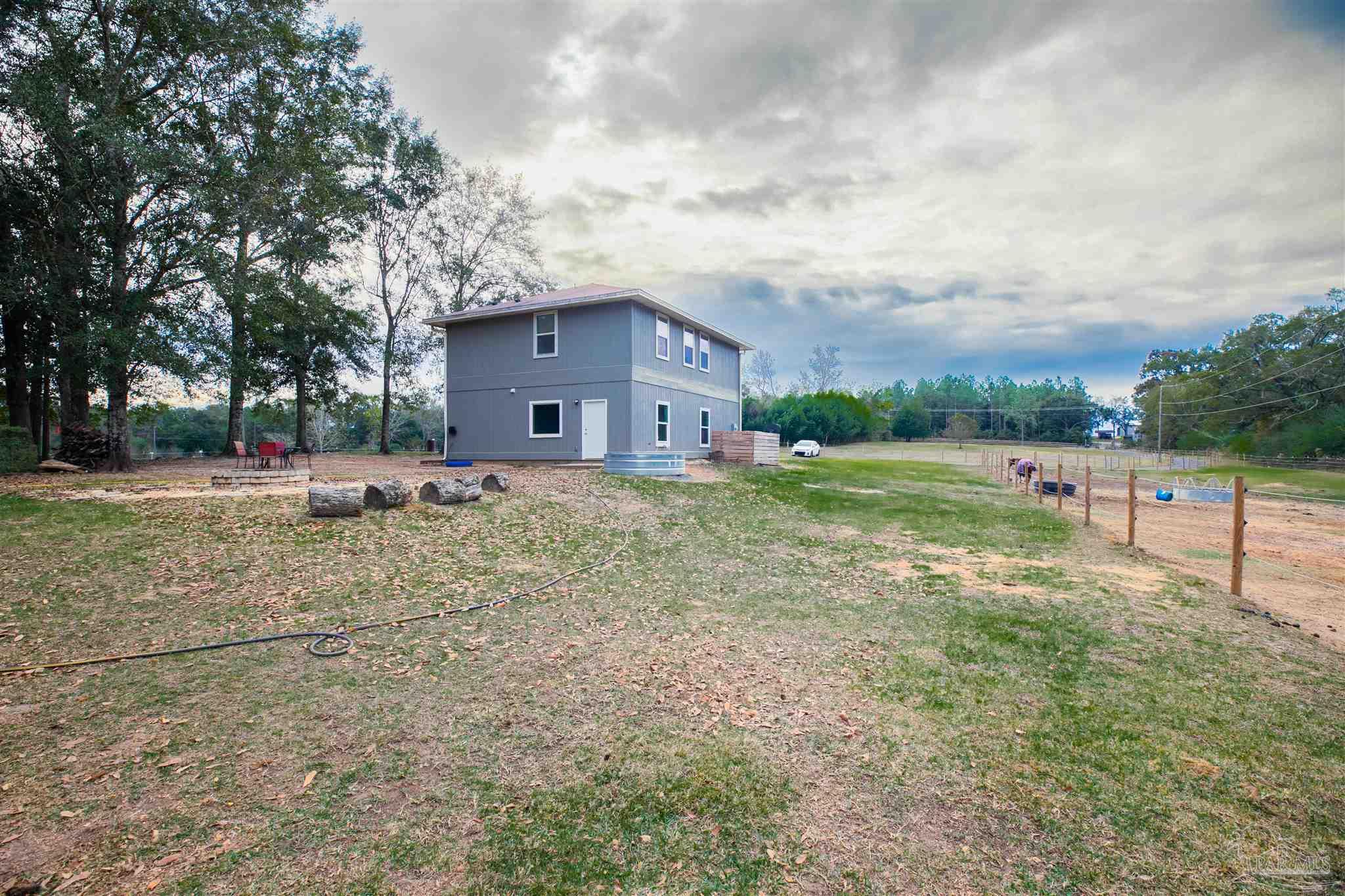 Two-story gray home with a fenced yard, outdoor seating, and a round metal stock tank.