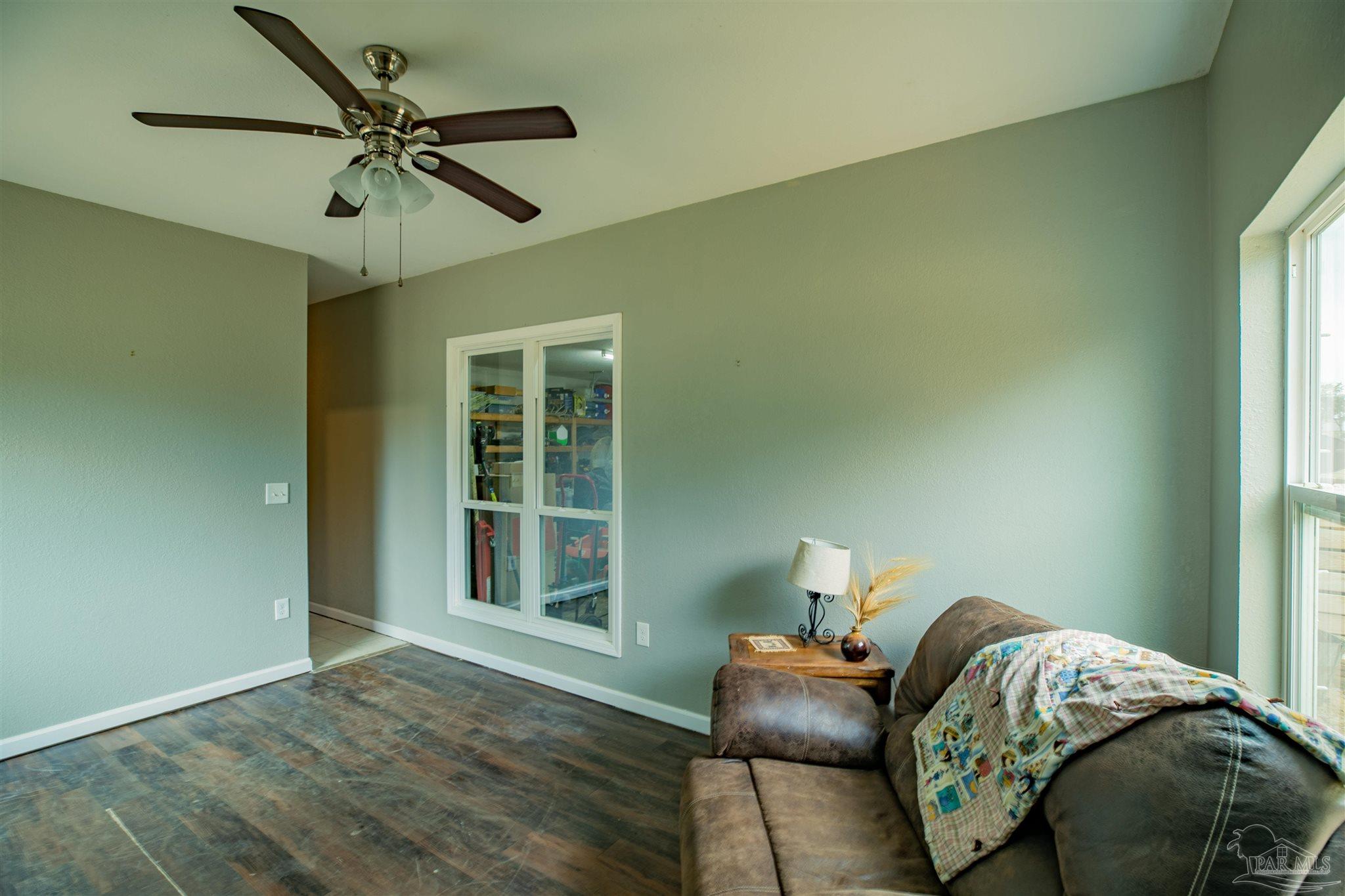 Bedroom with green walls, ceiling fan, dark flooring, and a brown sofa beside a tall window.