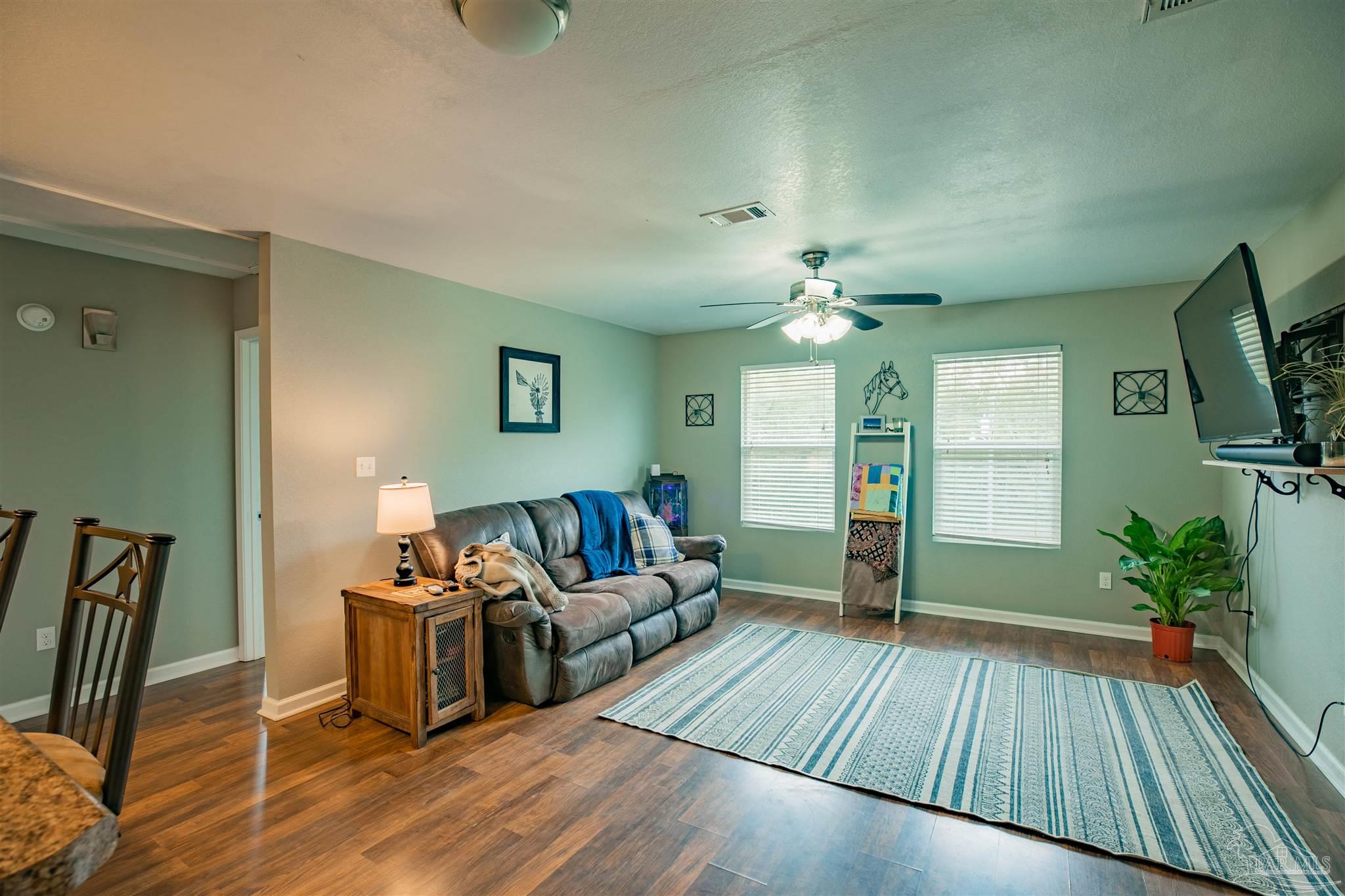 Living room with a gray sofa, ceiling fan, and blue-and-white rug on wood flooring.
