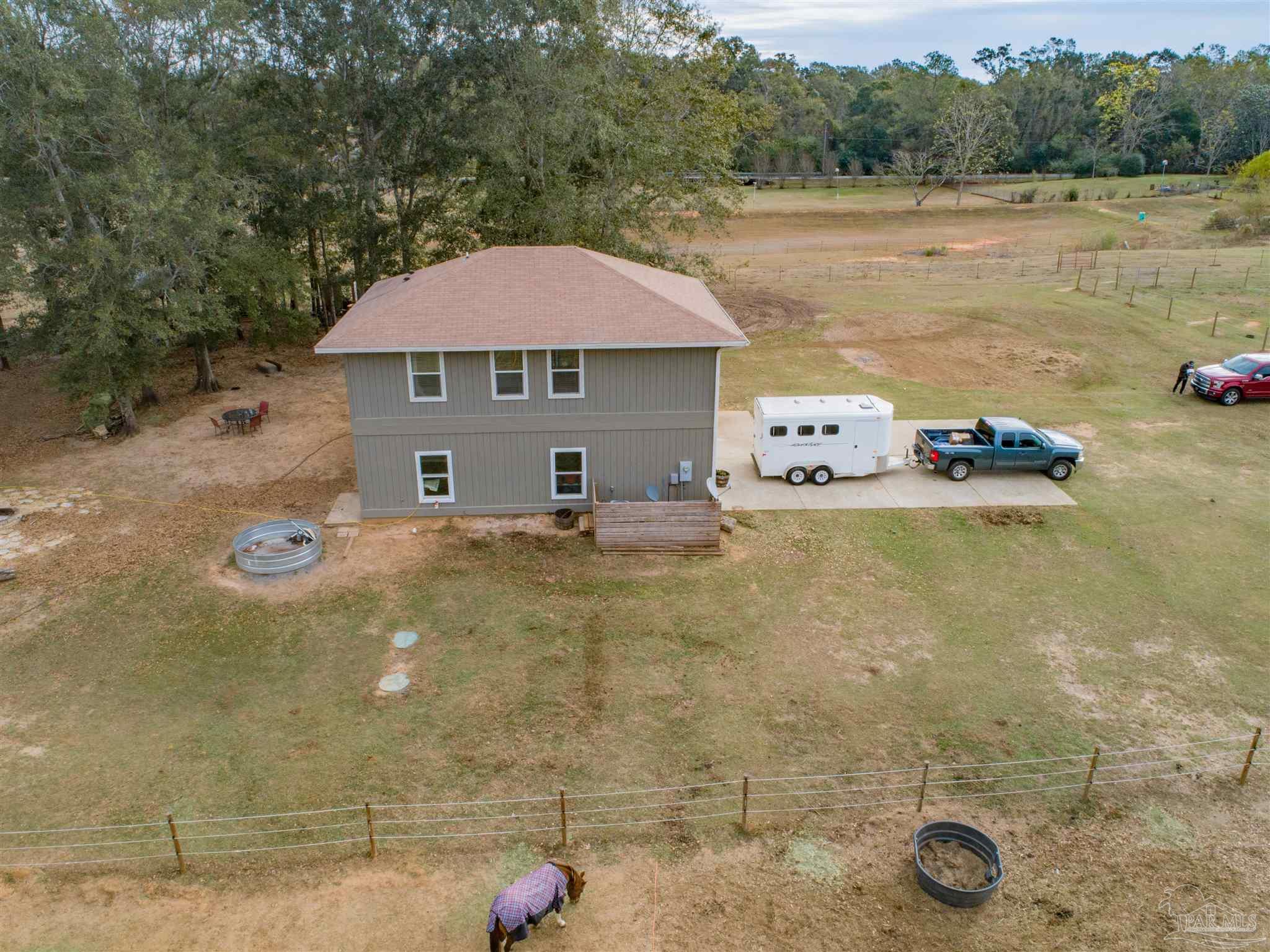 Aerial view of a gray two-story house, fenced pasture, and driveway with a horse trailer and pickup.
