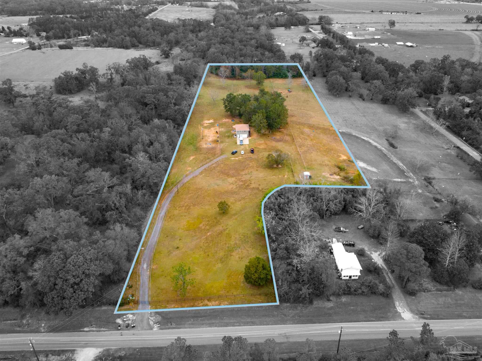 Aerial view of a rural property outlined in blue, with a small house, curving driveway, and open acreage.