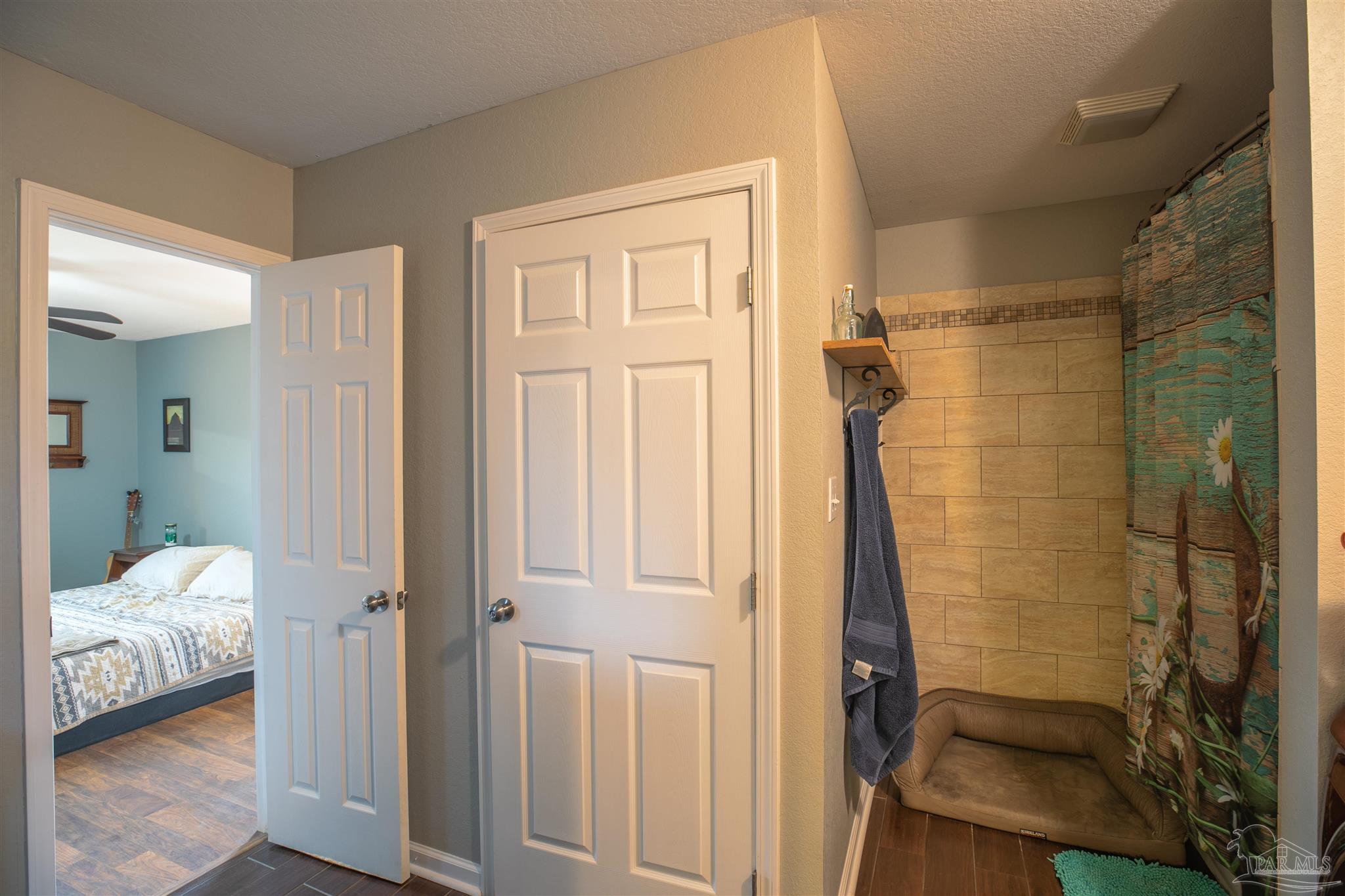 Bathroom with a tan tile shower and low wash basin beside an open bedroom doorway.