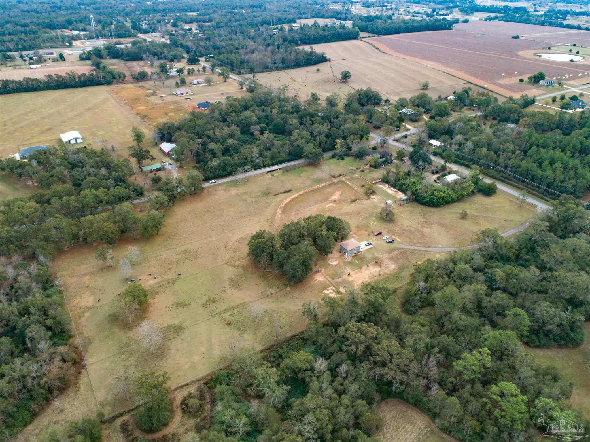 Aerial view of a rural home amid open acreage, wooded edges, and surrounding farmland.