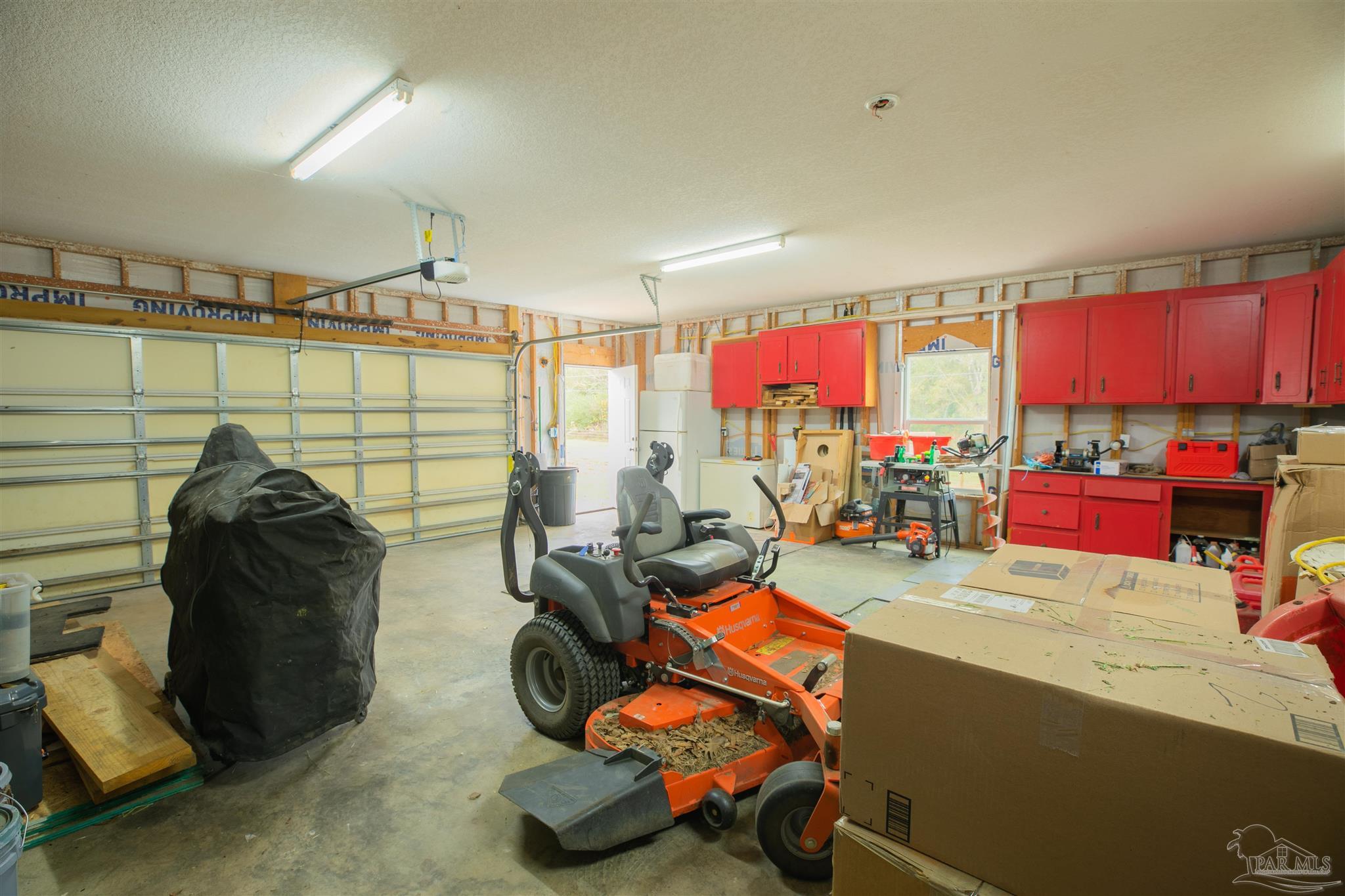 Garage workshop with red cabinets, tools, boxes, and an orange riding mower.