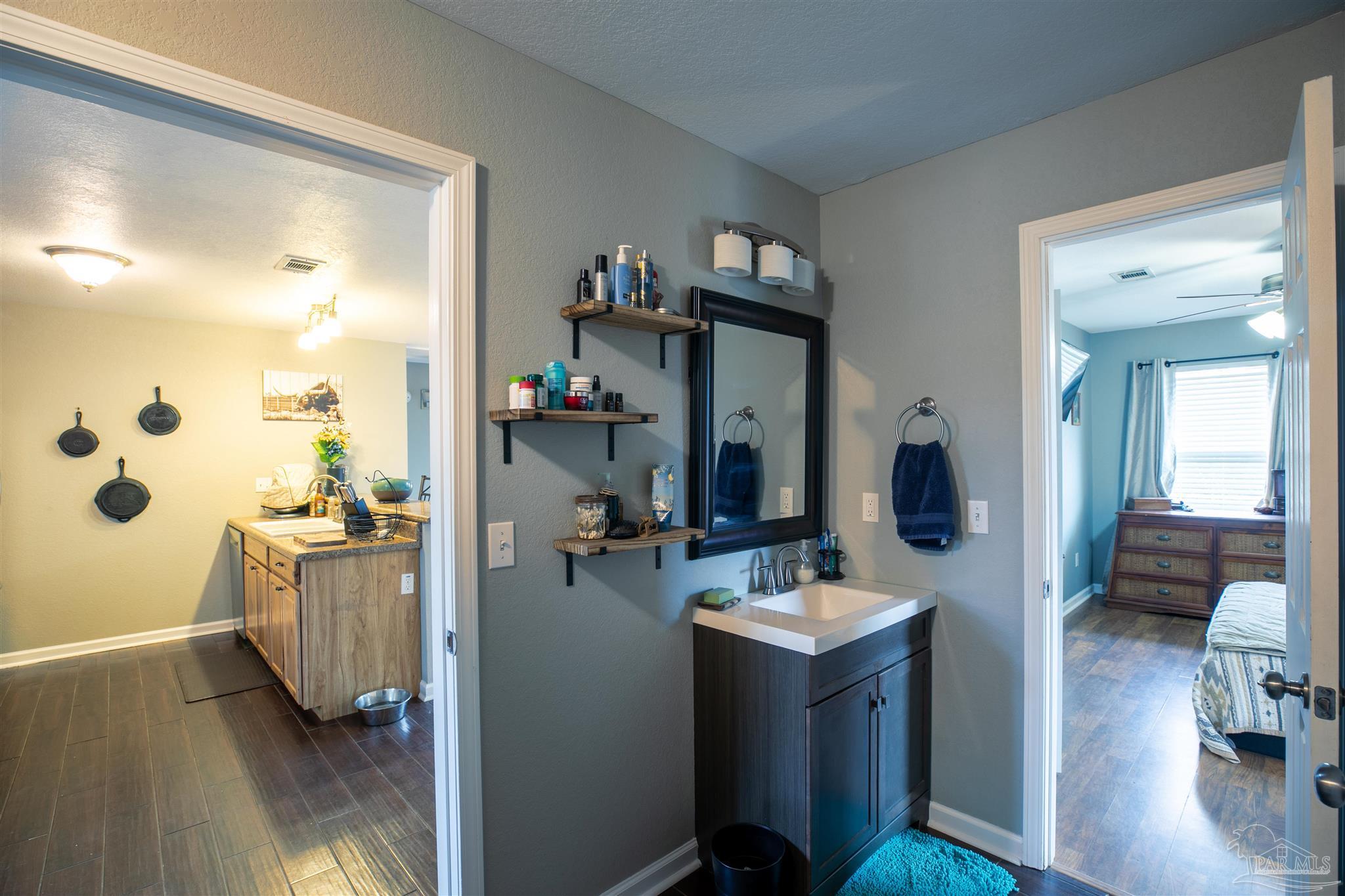 Bathroom vanity with white sink, dark cabinetry, wall mirror, and open shelves beside a bedroom doorway.