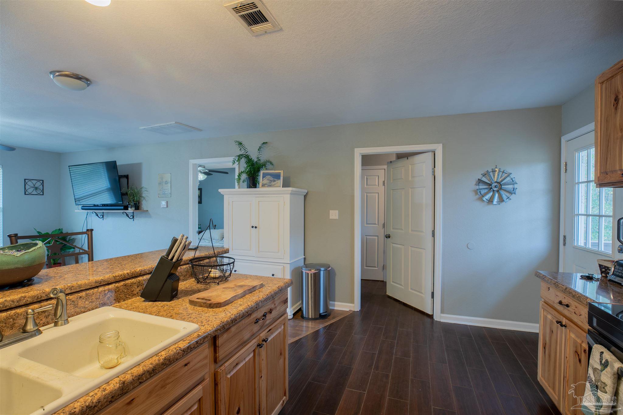 Kitchen with granite countertops, wood cabinetry, a double sink, and dark plank flooring.