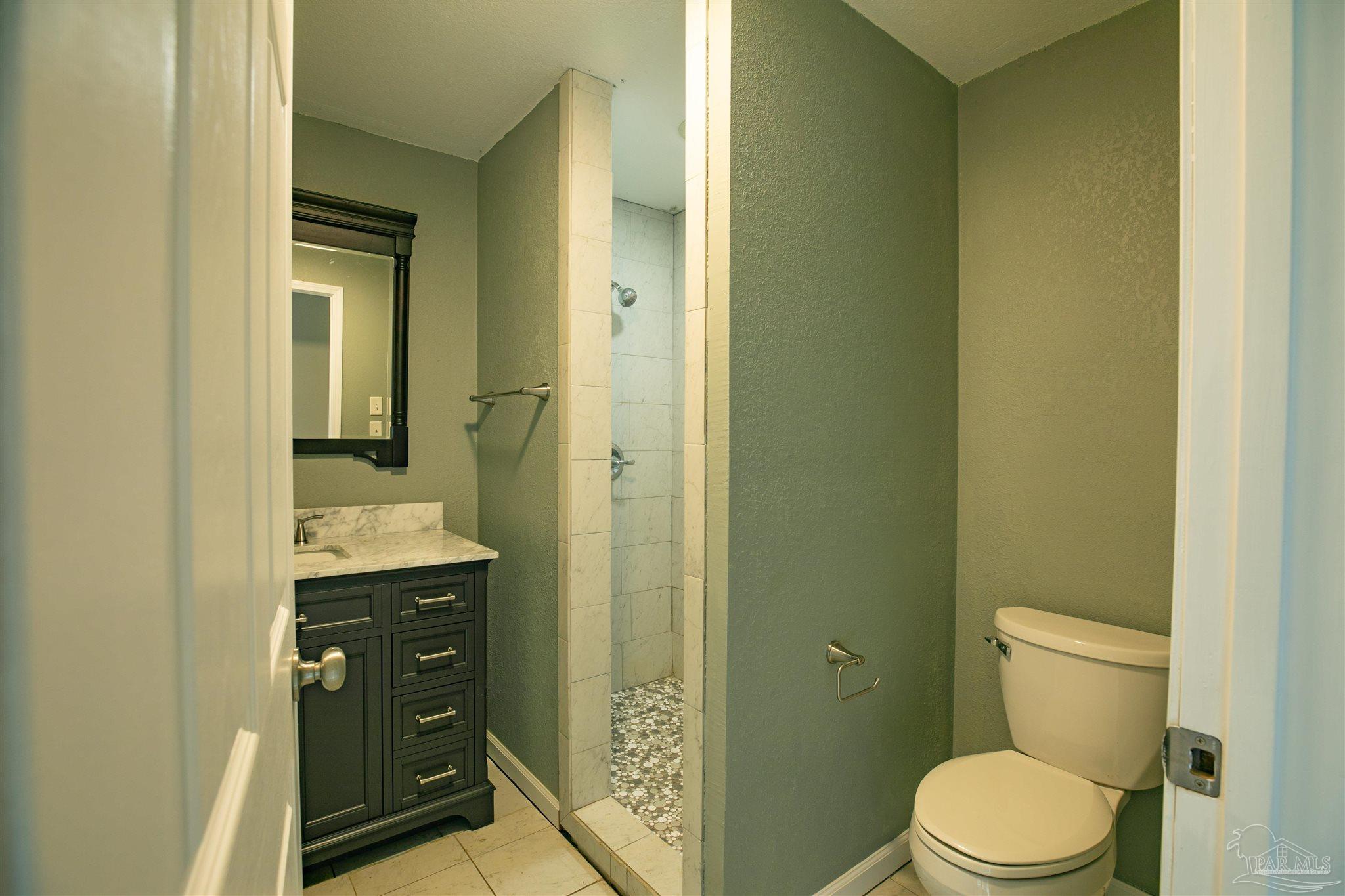 Bathroom with a dark vanity, marble countertop, and tiled walk-in shower beside the toilet.
