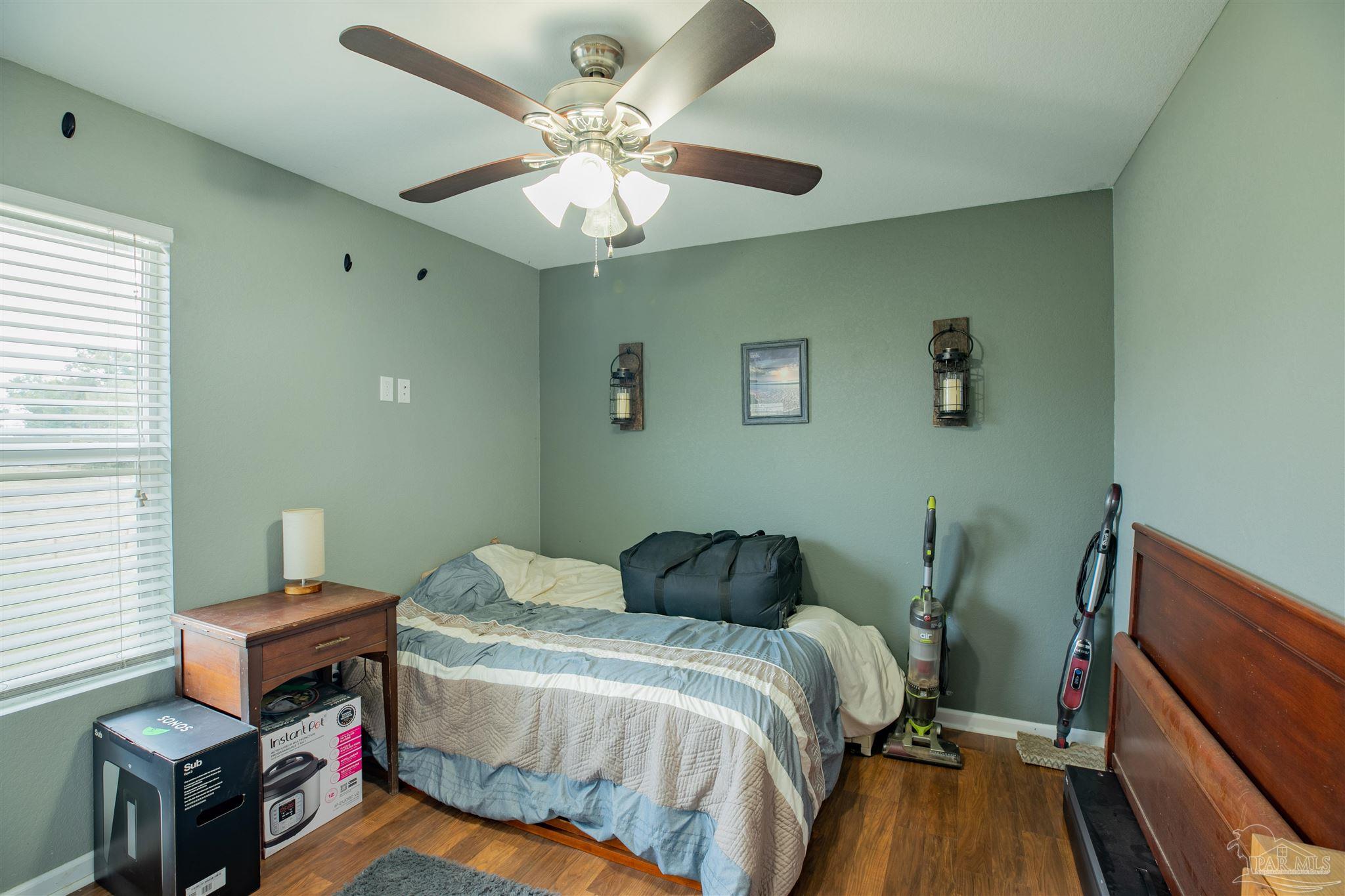 Bedroom with blue-and-cream bedding, green walls, hardwood floors, and vacuums beside the bed.