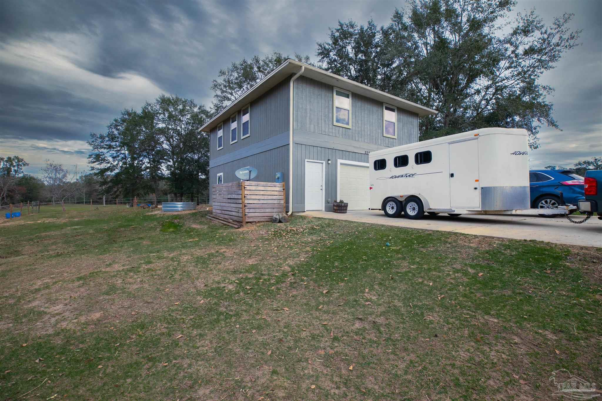 Two-story gray house with a broad grassy yard and a white horse trailer parked beside it.