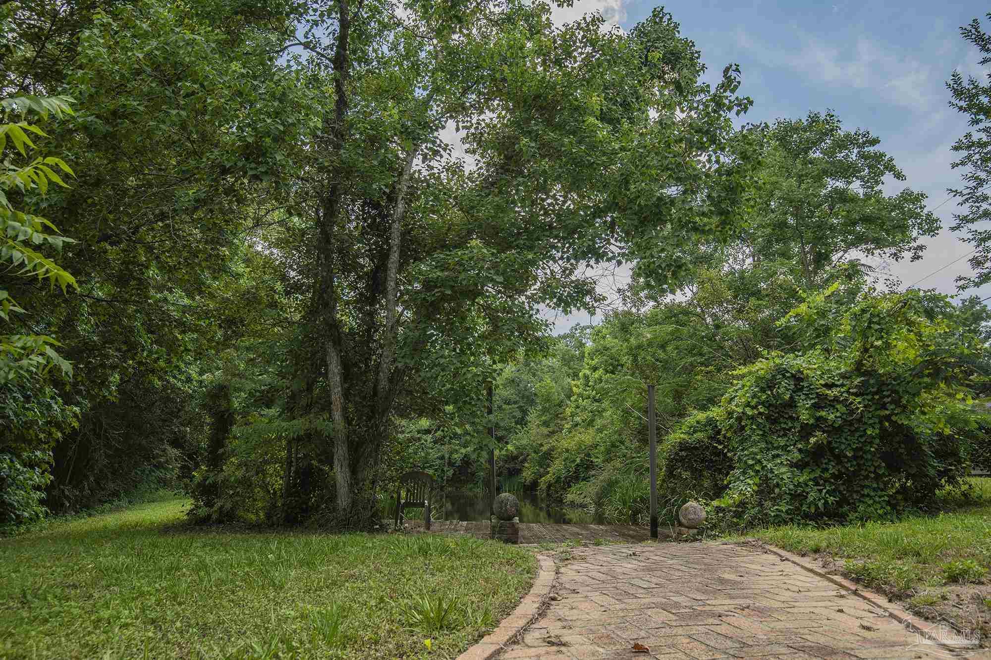 Paved path leads through a lush, wooded yard toward a small gate.