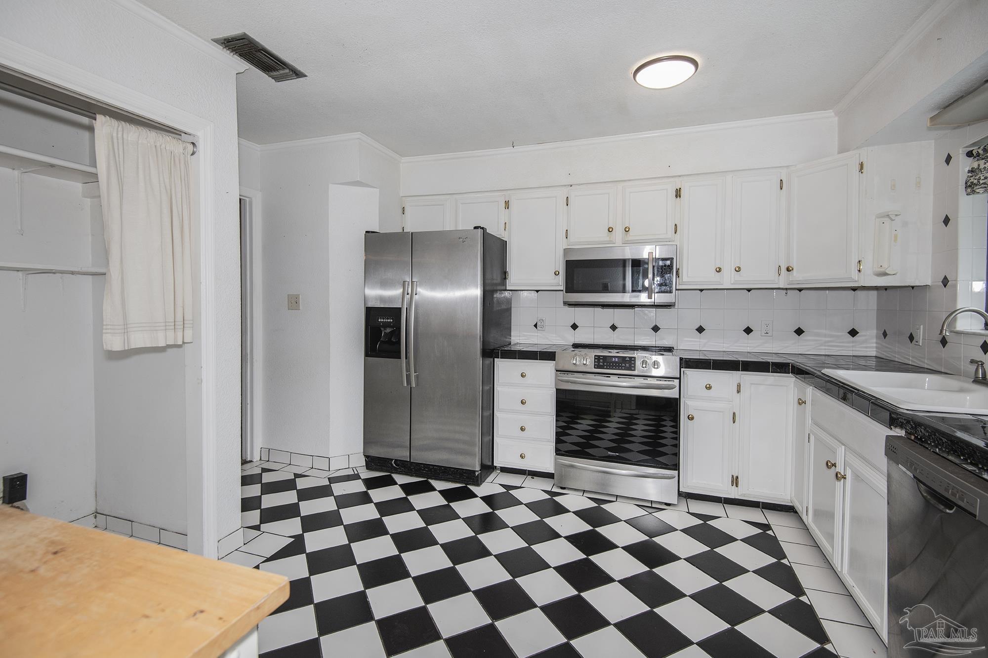 Kitchen with stainless steel appliances, white cabinets, and a black-and-white checkerboard floor.