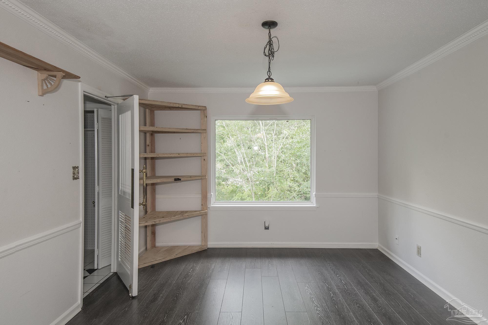 Vacant room with dark plank flooring, wooden built-in shelves, and a large window overlooking trees.