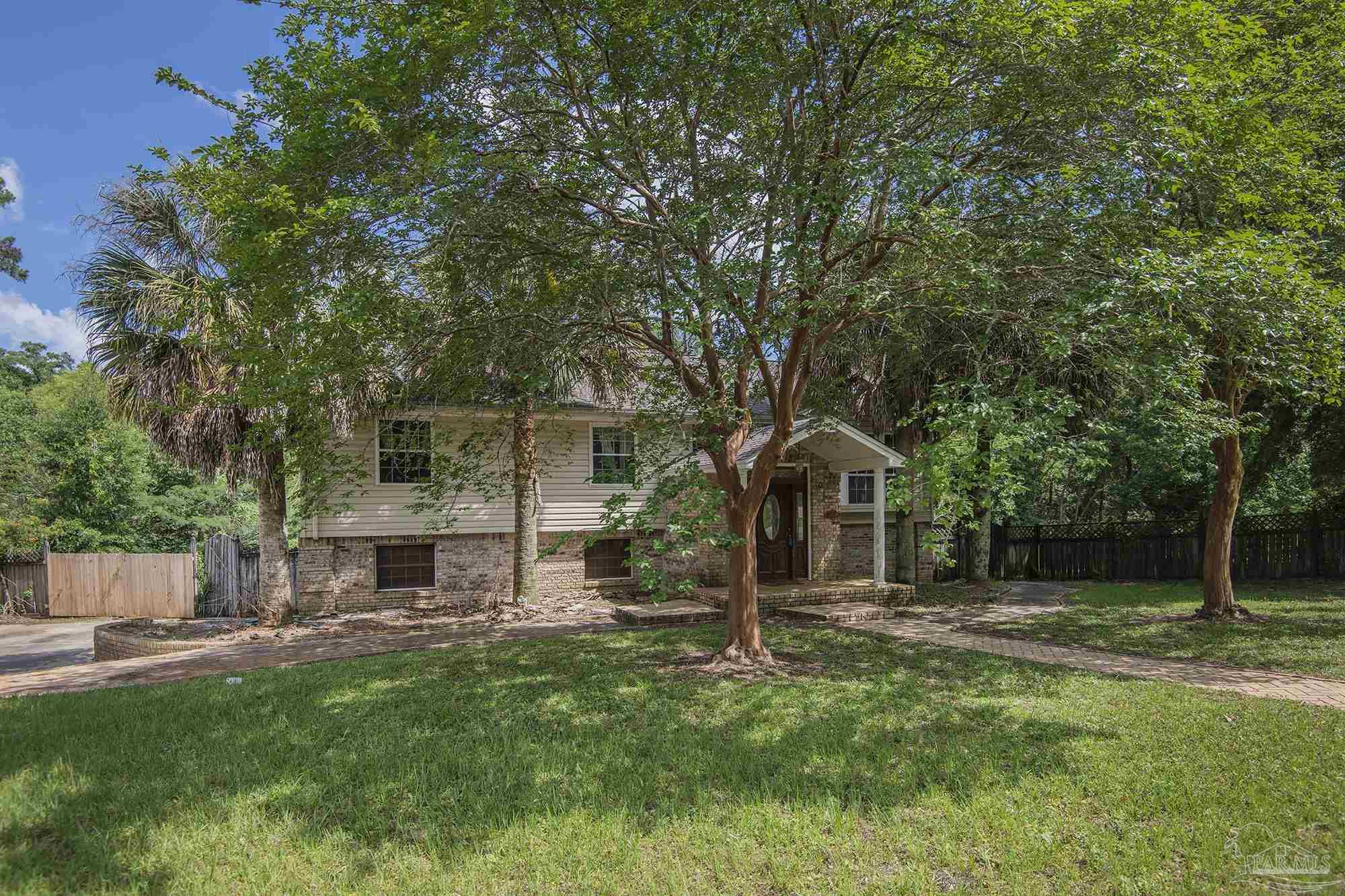 Split-level home with a brick lower facade and covered entry beneath mature trees.